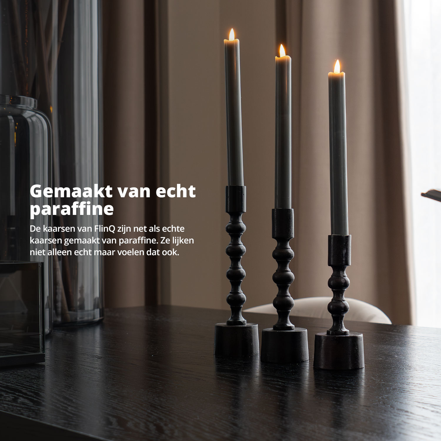 Three gray candles in black holders are displayed on a black table.