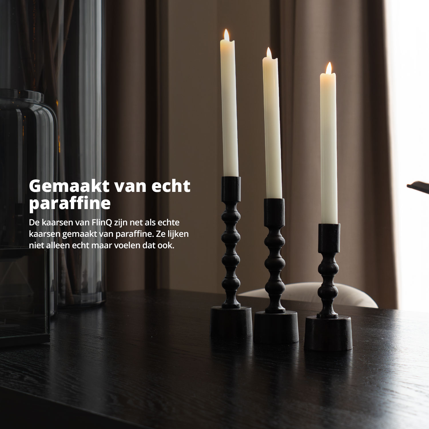 Three lit paraffin candles in black holders on a black table.