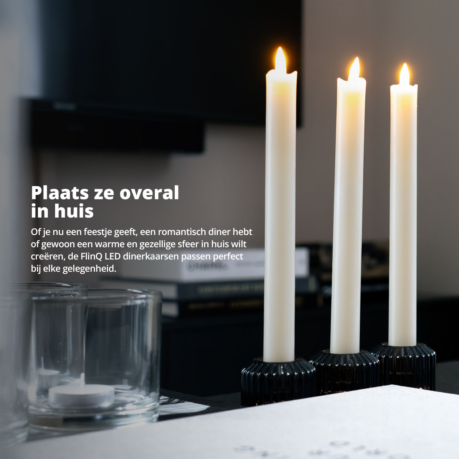 Three white candles on a black surface with a glass candle holder in the foreground.