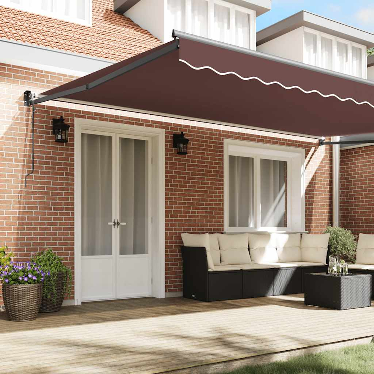 Una tenda da sole marrone copre un patio con mobili su una terrazza in legno accanto a un edificio in mattoni.