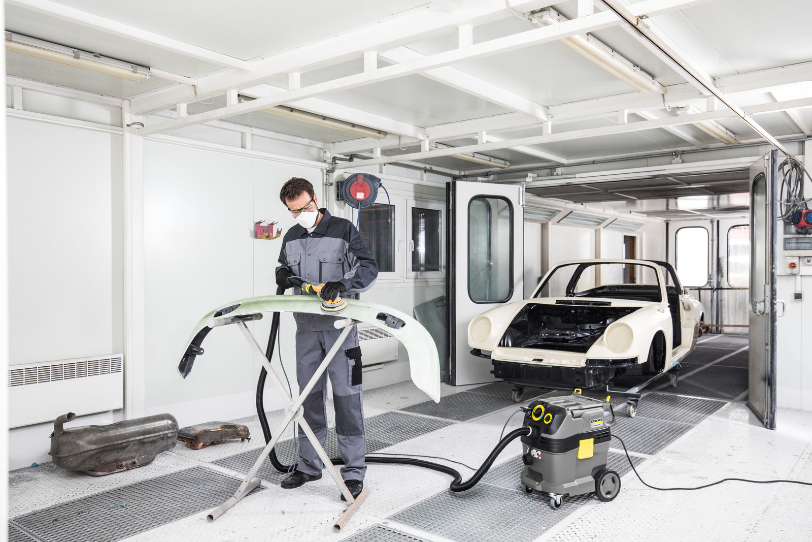 Ein Arbeiter schleift eine Stoßstange in einer Garage mit einem gelben Staubsauger.