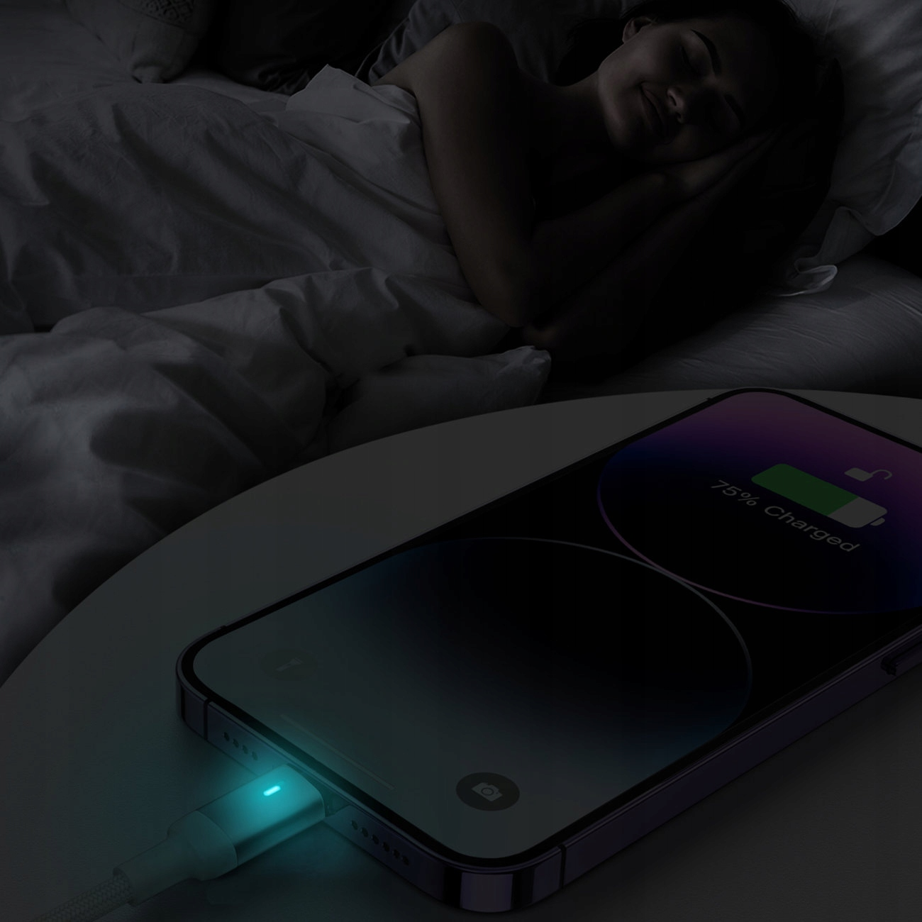 Telefon ładuje się na stoliku nocnym. Kobieta śpi w tle. Telefon pokazuje 75% naładowania.