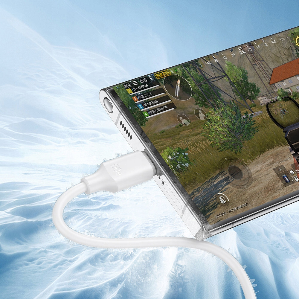 Telefon jest ładowany białym kablem. Na ekranie wyświetlana jest gra mobilna. Scena ma śnieg.