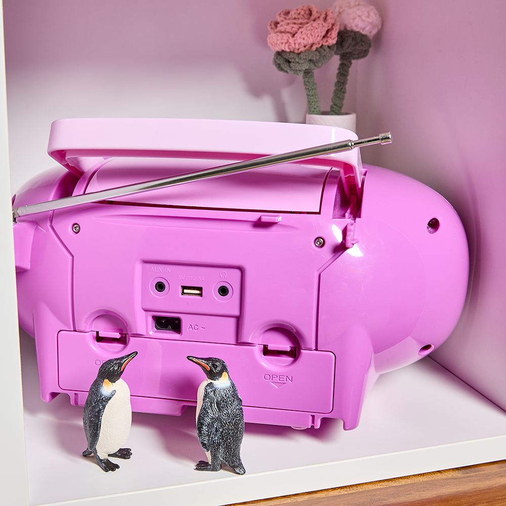 Pinkfarbene Boombox auf einem Regal. Zwei Pinguinfiguren stehen davor.