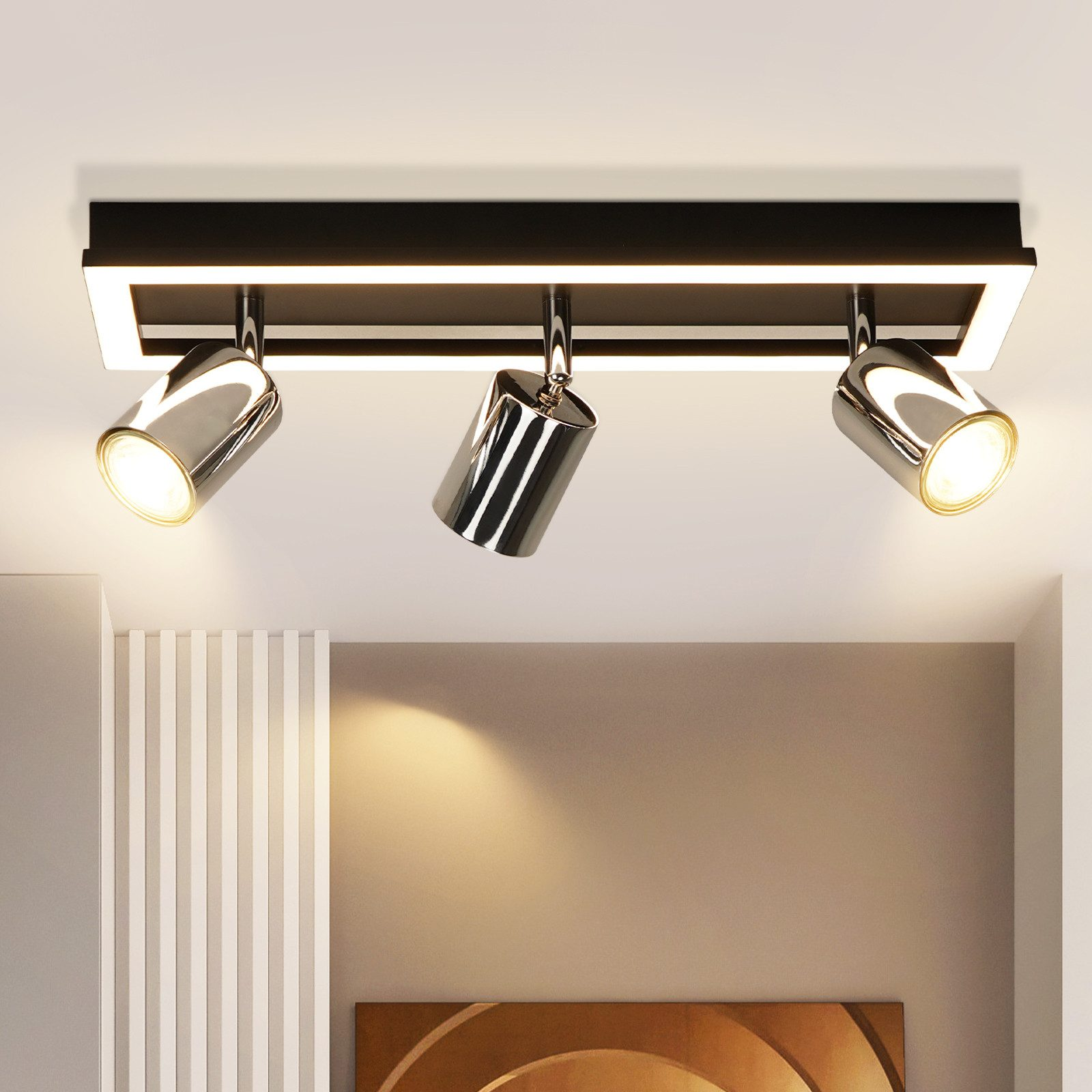 Tre faretti cromati illuminano una stanza moderna, con un apparecchio bianco e nero e opere d'arte sulla parete.