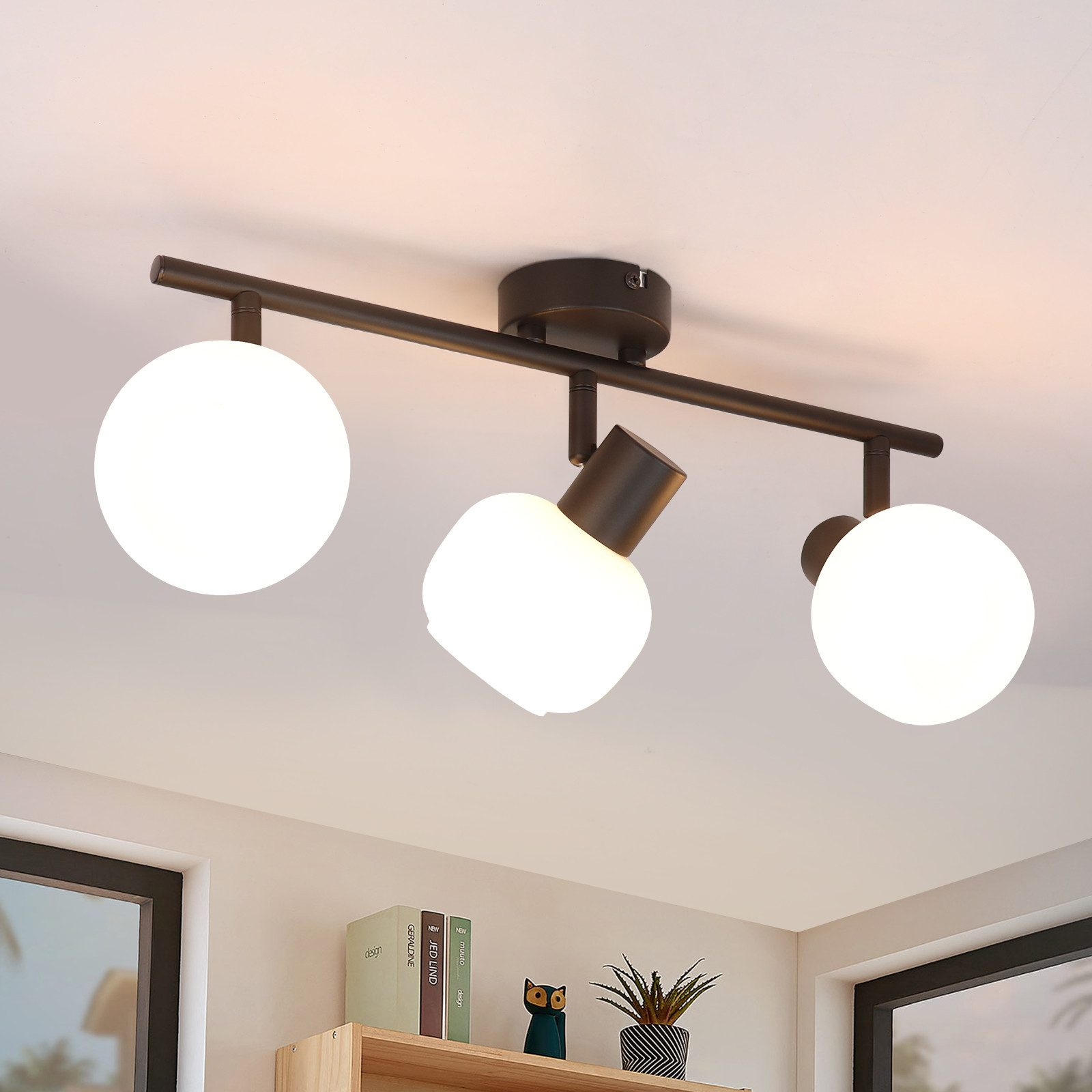 Lampada da soffitto con tre luci rotonde bianche. La lampada è nera e montata su un soffitto bianco.