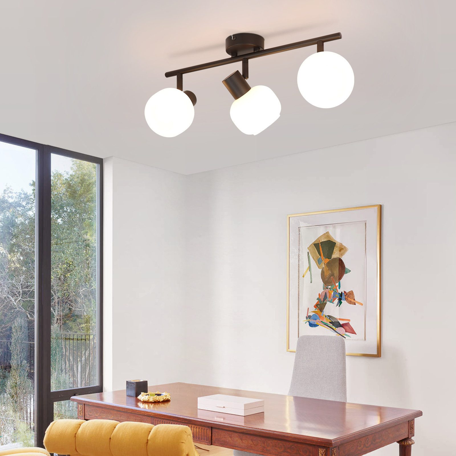 Lampada da soffitto con tre luci rotonde bianche. Scrivania e dipinto sullo sfondo, in una stanza ben illuminata.