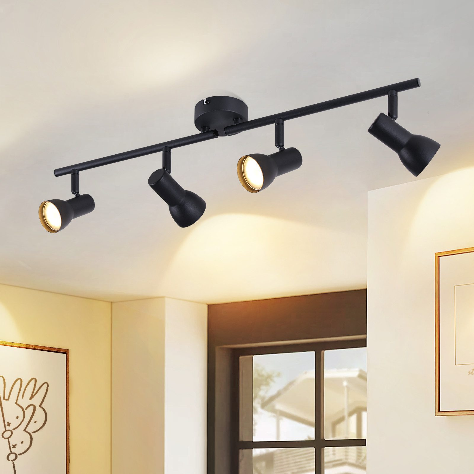 Apparecchio di illuminazione a binario nero con quattro faretti regolabili. Le luci hanno interni dorati e sono accese.