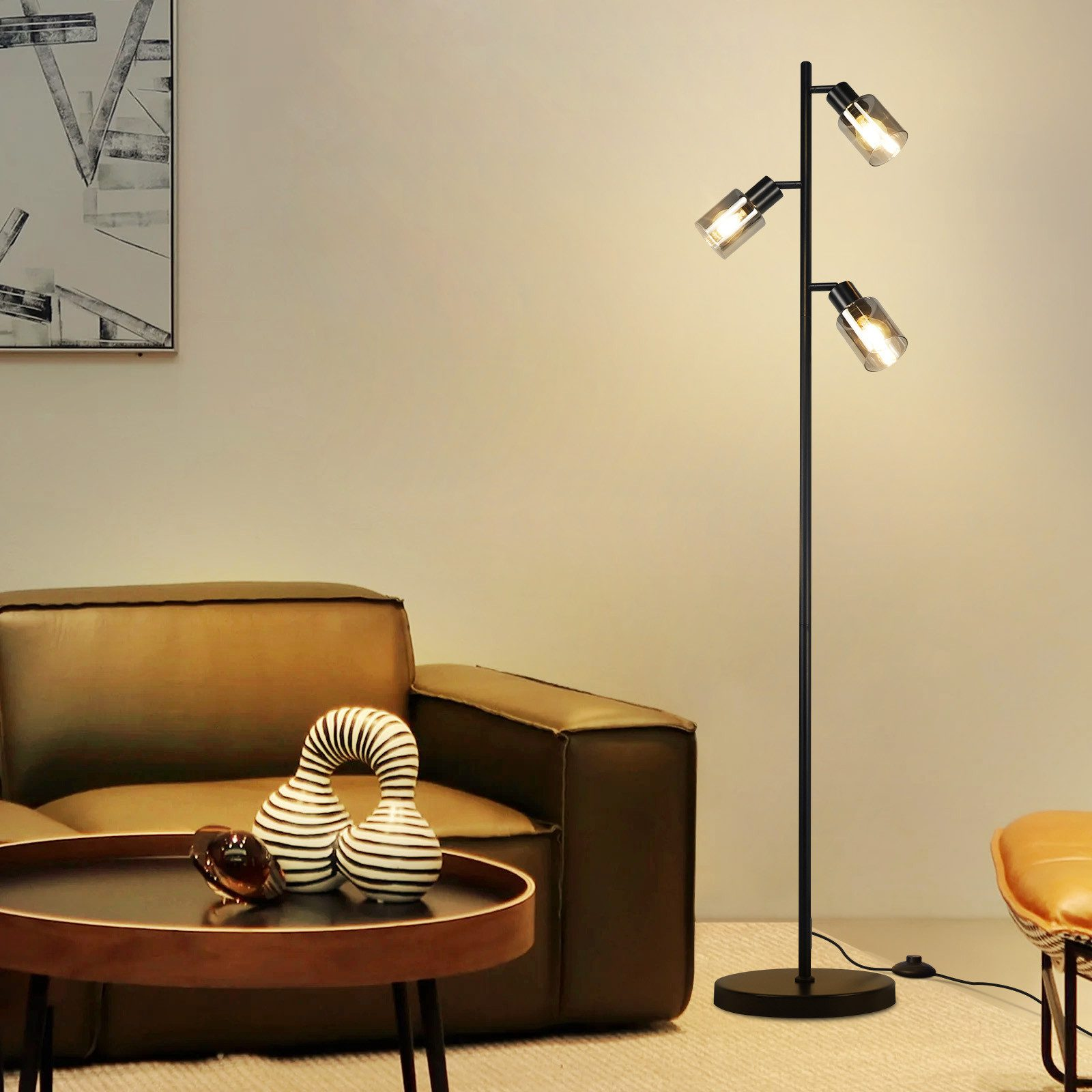 Czarna lampa podłogowa z trzema światłami, ciemny drewniany stolik kawowy z dekoracjami i brązowa skórzana sofa w pokoju.