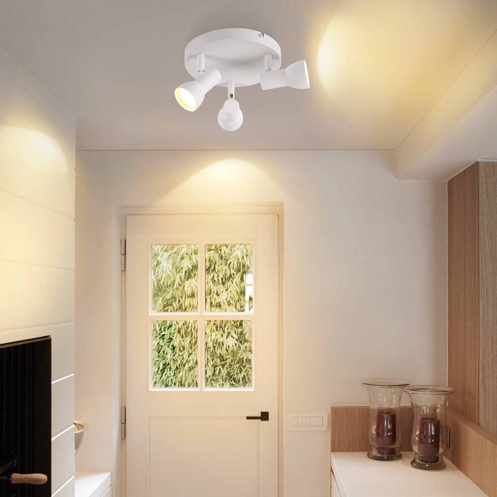 Lampada da soffitto con tre faretti bianchi regolabili. Una porta con finestra di vetro sullo sfondo.