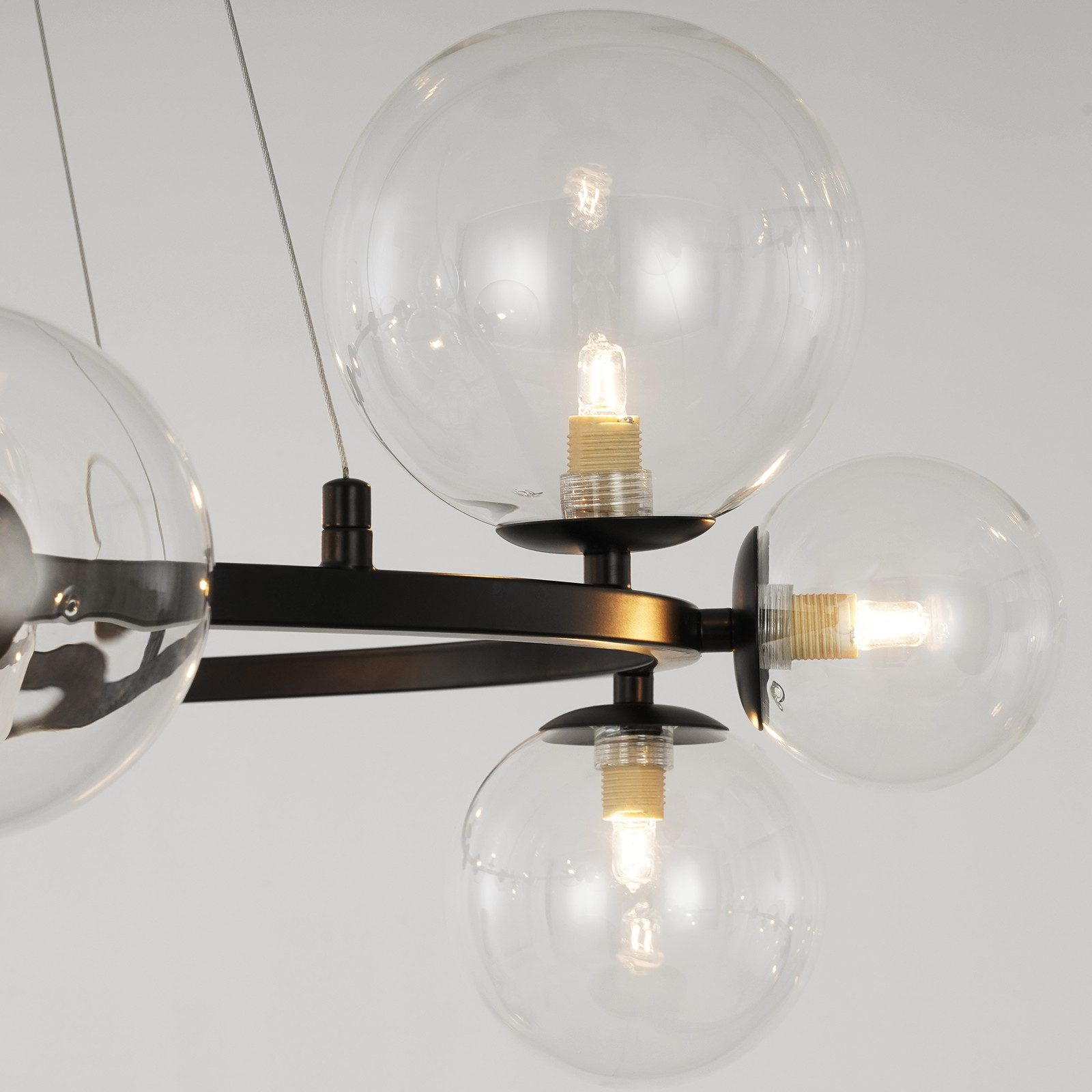 Un primo piano mostra i globi in vetro trasparente e la struttura in metallo nero di un lampadario su sfondo bianco.