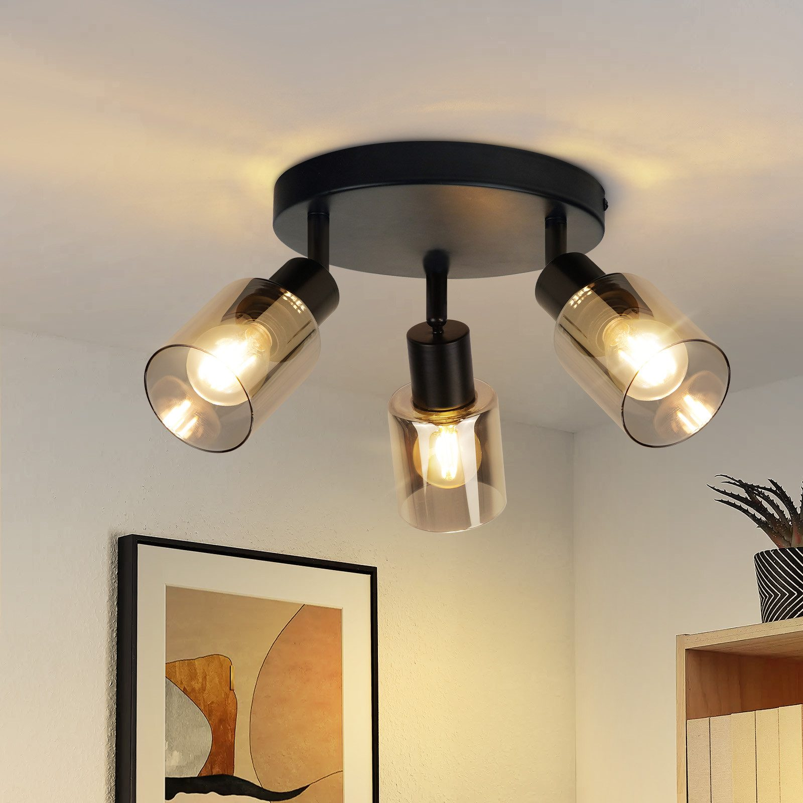 Una plafoniera a tre lampadine illumina una stanza con un dipinto e una mensola sullo sfondo.