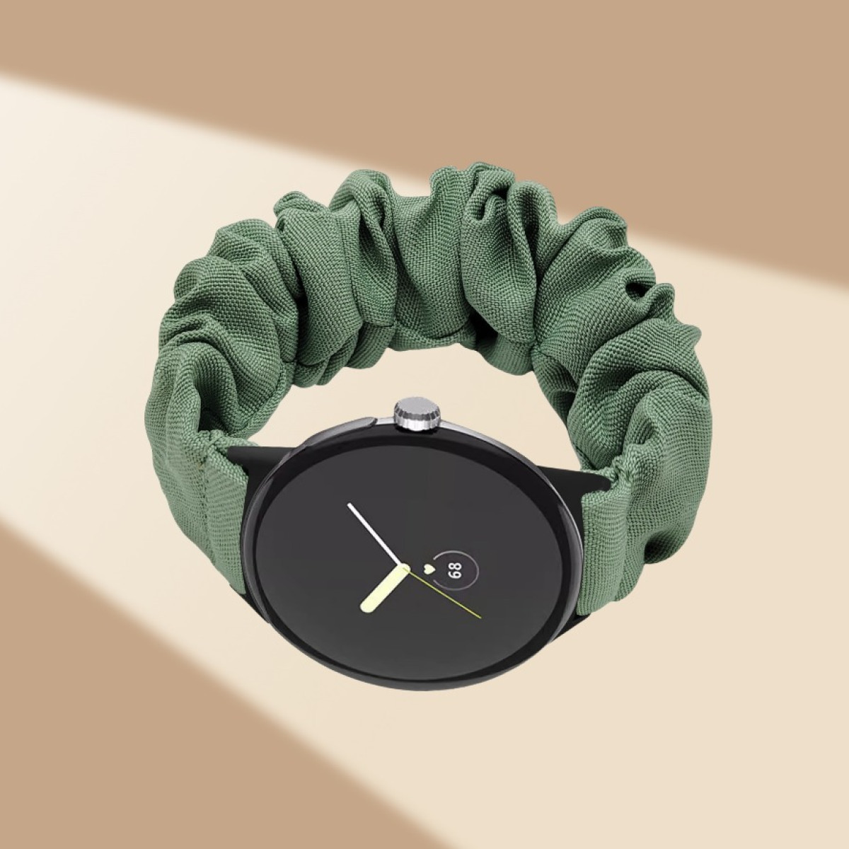 Uno smartwatch nero con un cinturino a scrunchie in tessuto verde su uno sfondo beige.
