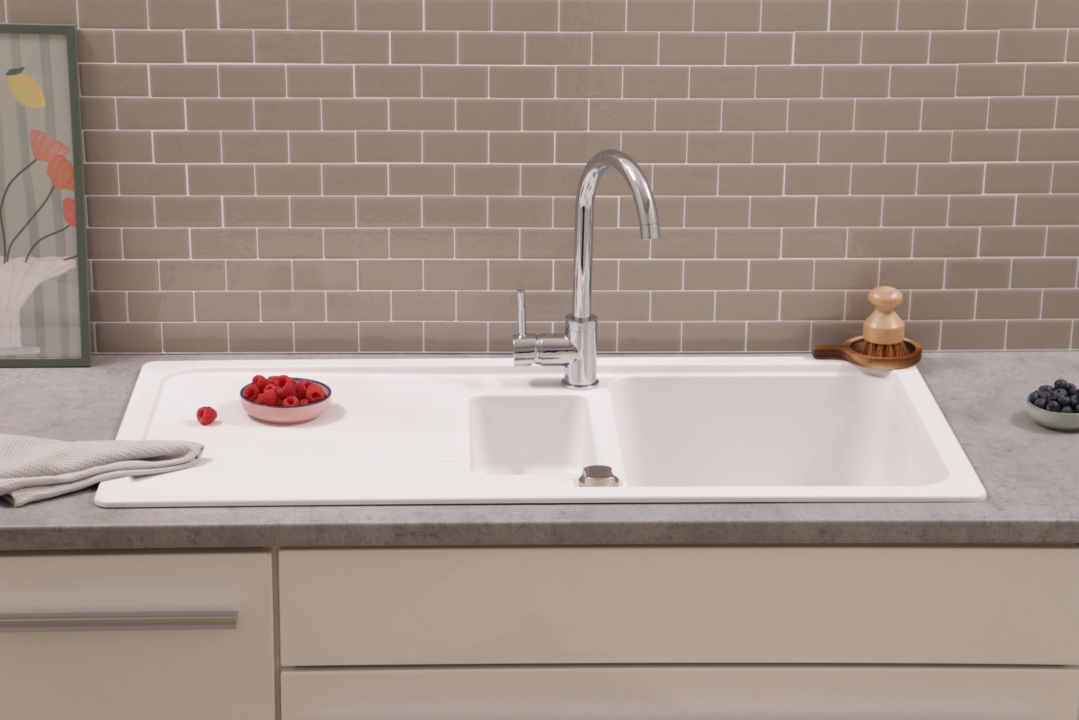 Ein weißes Küchenspülbecken mit Chromhahn, Himbeeren und Blaubeeren auf einer grauen Arbeitsplatte.