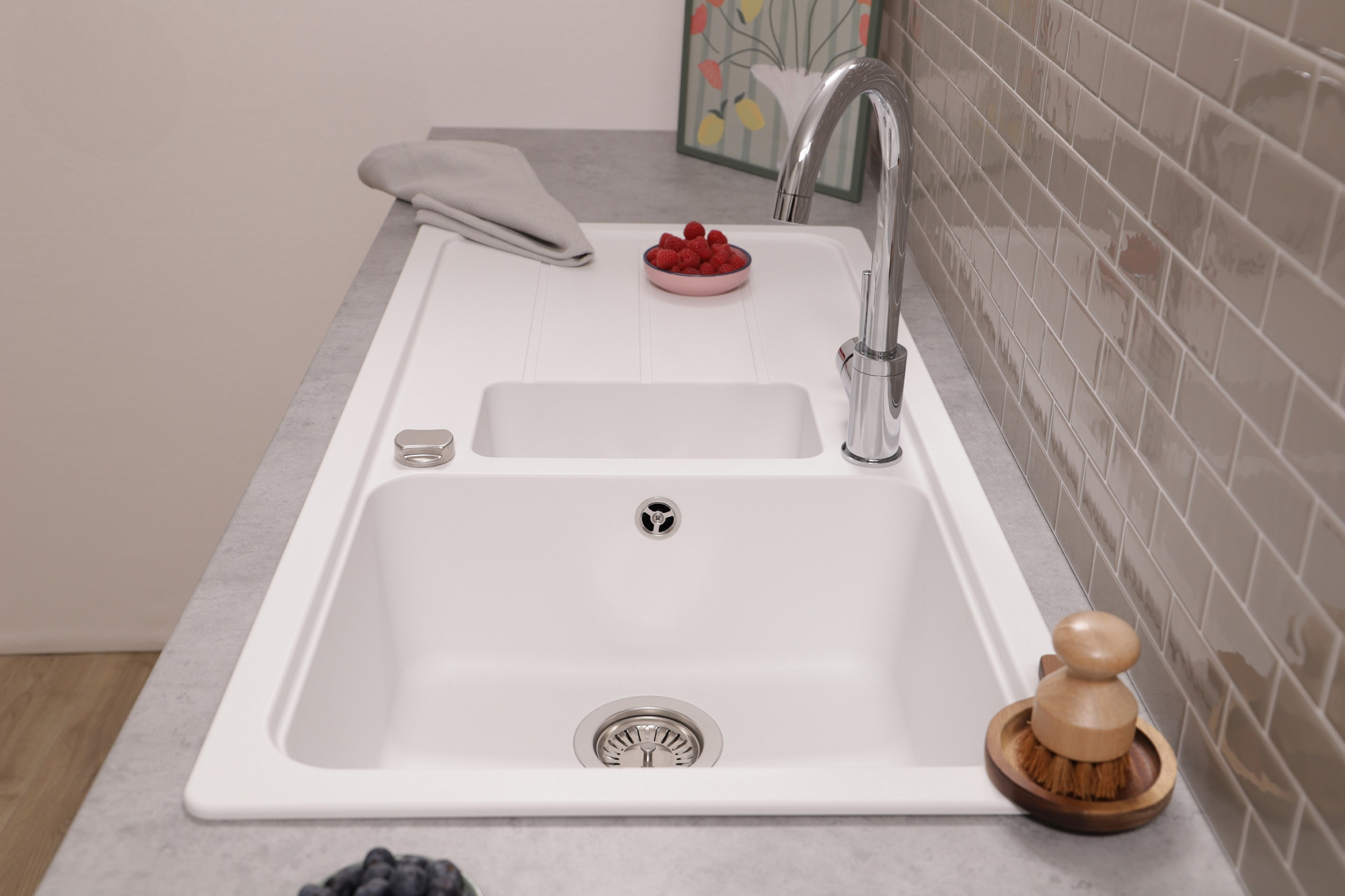 Ein weißes Küchenspülbecken mit einem Chromhahn, Himbeeren und Blaubeeren auf einer grauen Arbeitsplatte.