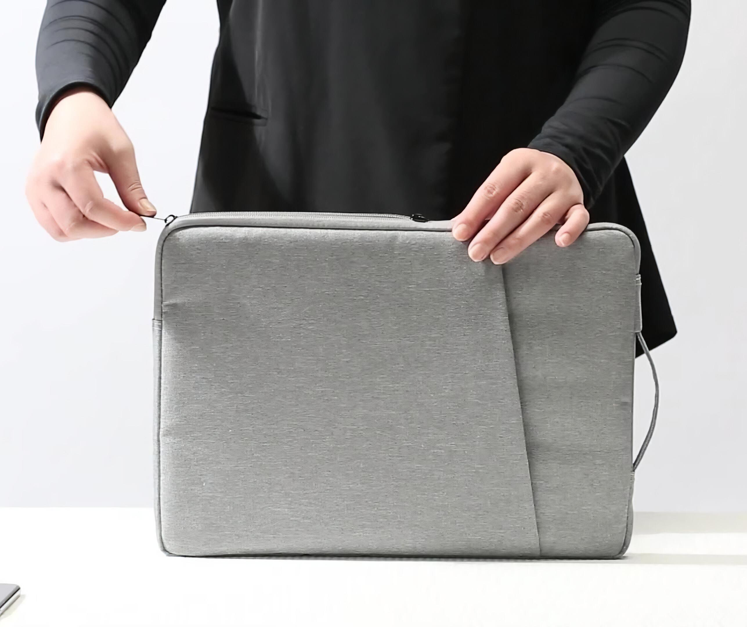 Person, die eine graue Laptoptasche zuzieht und vor einem weißen Hintergrund steht, um den Verschluss der Tasche zu demonstrieren.