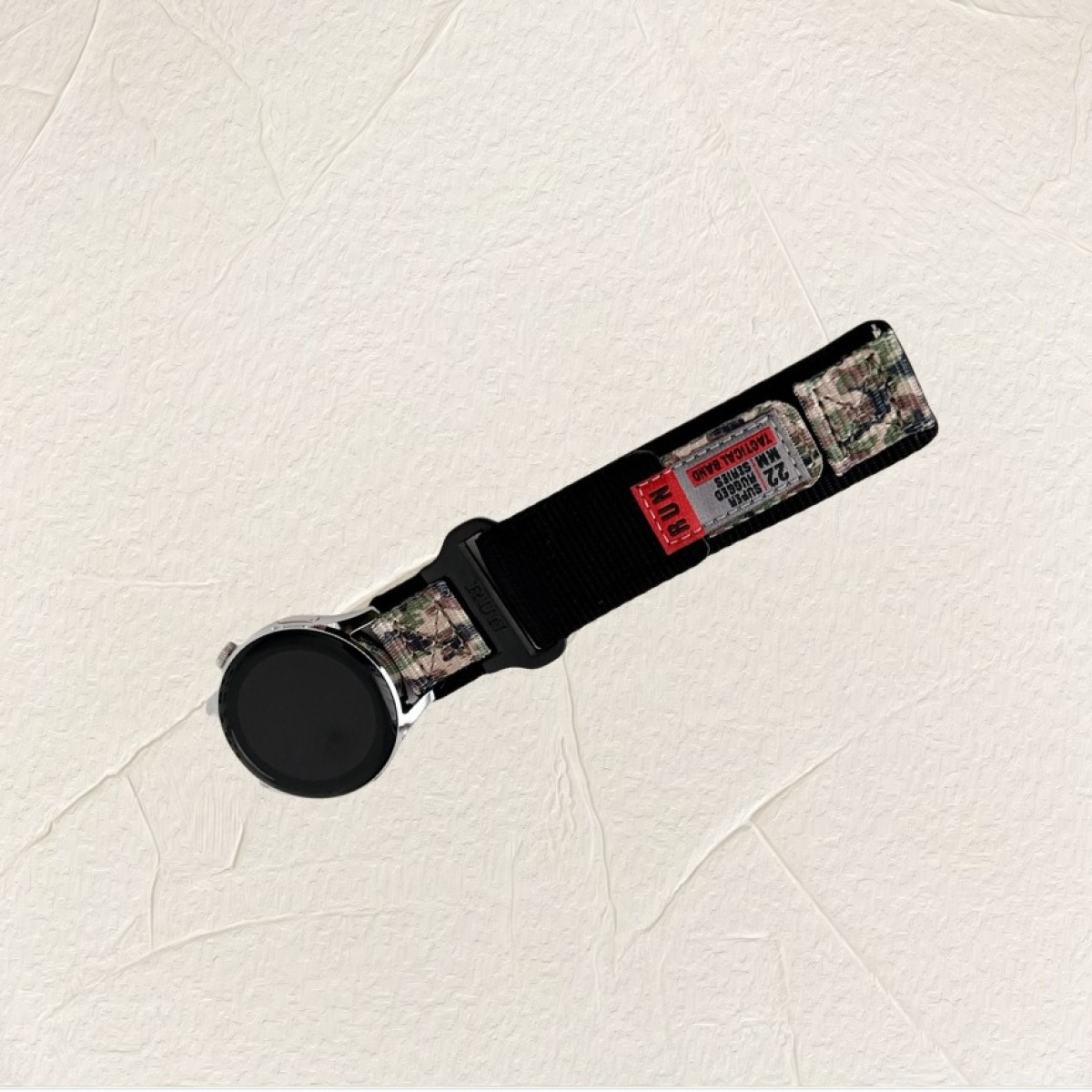 Smartwatch con cinturino tattico in nylon nero su sfondo bianco con ombre di fogliame.