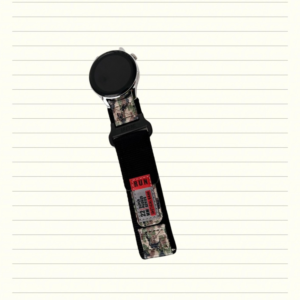 Smartwatch con cinturino tattico in nylon nero, inserti mimetici ed etichetta rossa 'RUN' su carta a righe.