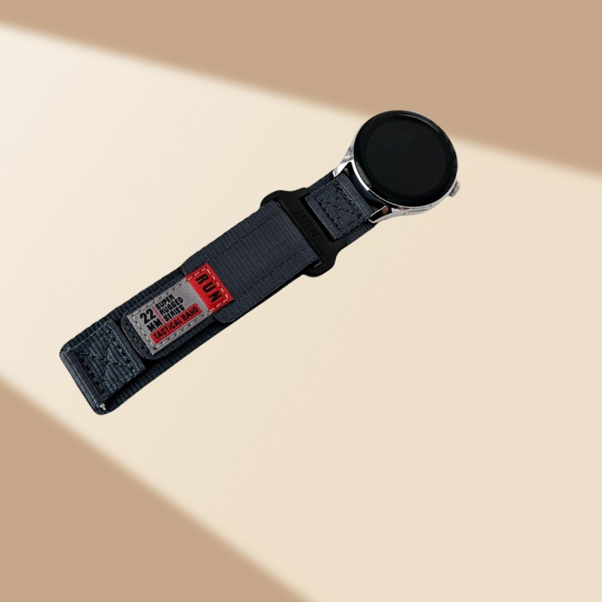 Eine graue Uhr mit einem Nylonarmband wird vor einem abgestuften beigen Hintergrund angezeigt.