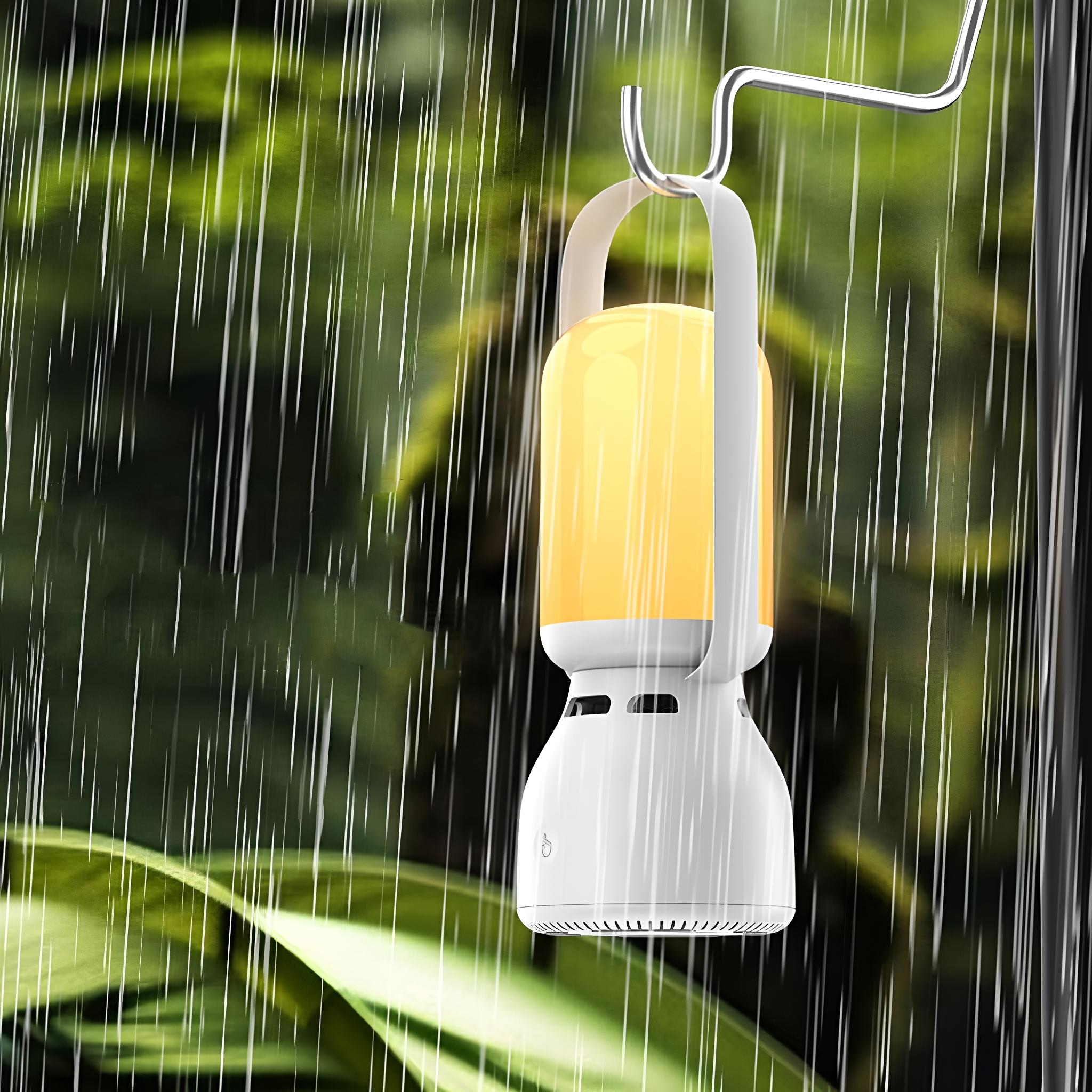 Eine weiße Lampe mit gelbem Schein hängt im Regen, mit verschwommenem grünen Hintergrund aus Blättern.