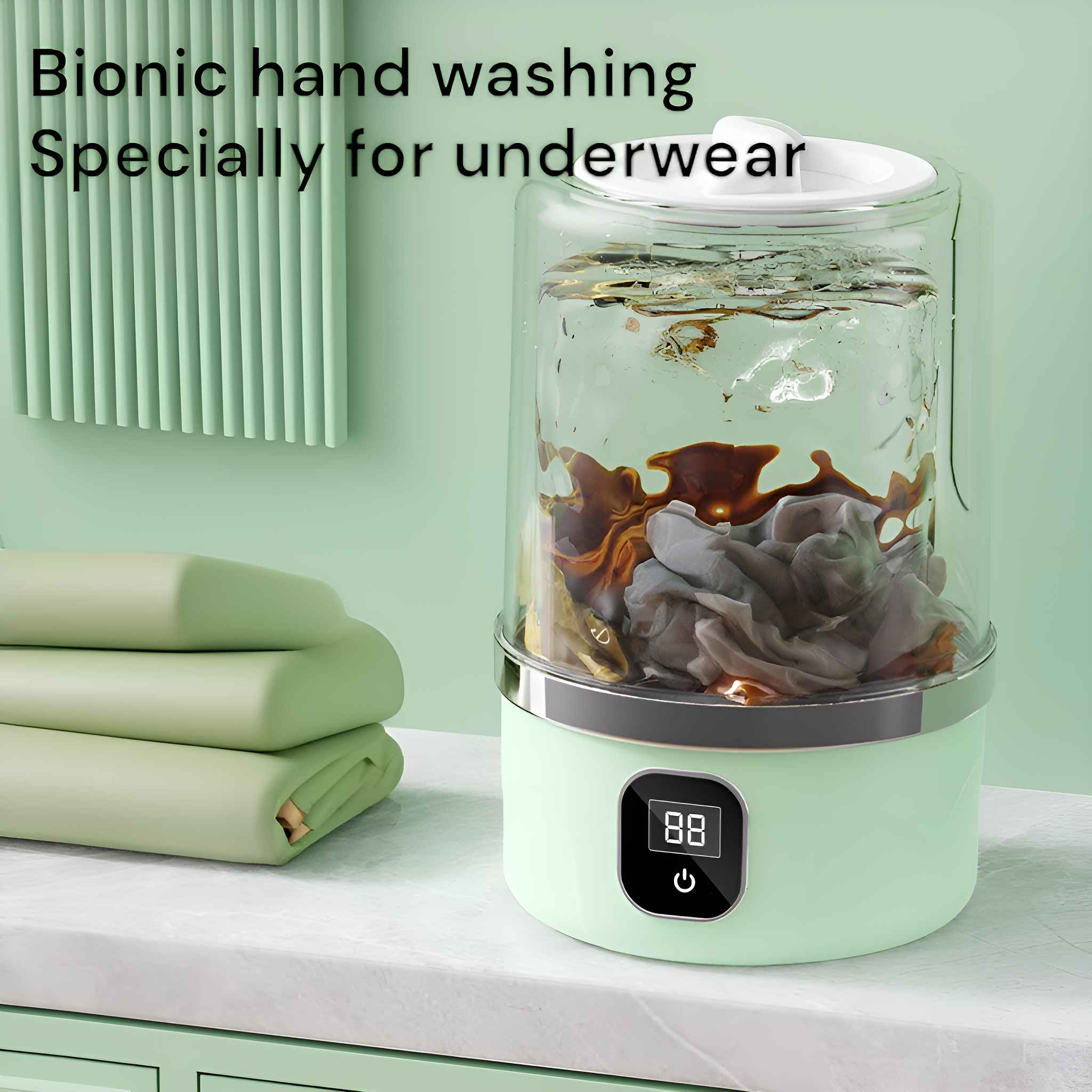 Kleine, grüne Mini-Waschmaschine mit Wasser und Kleidung gefüllt. Stapel grüner Handtücher daneben.
