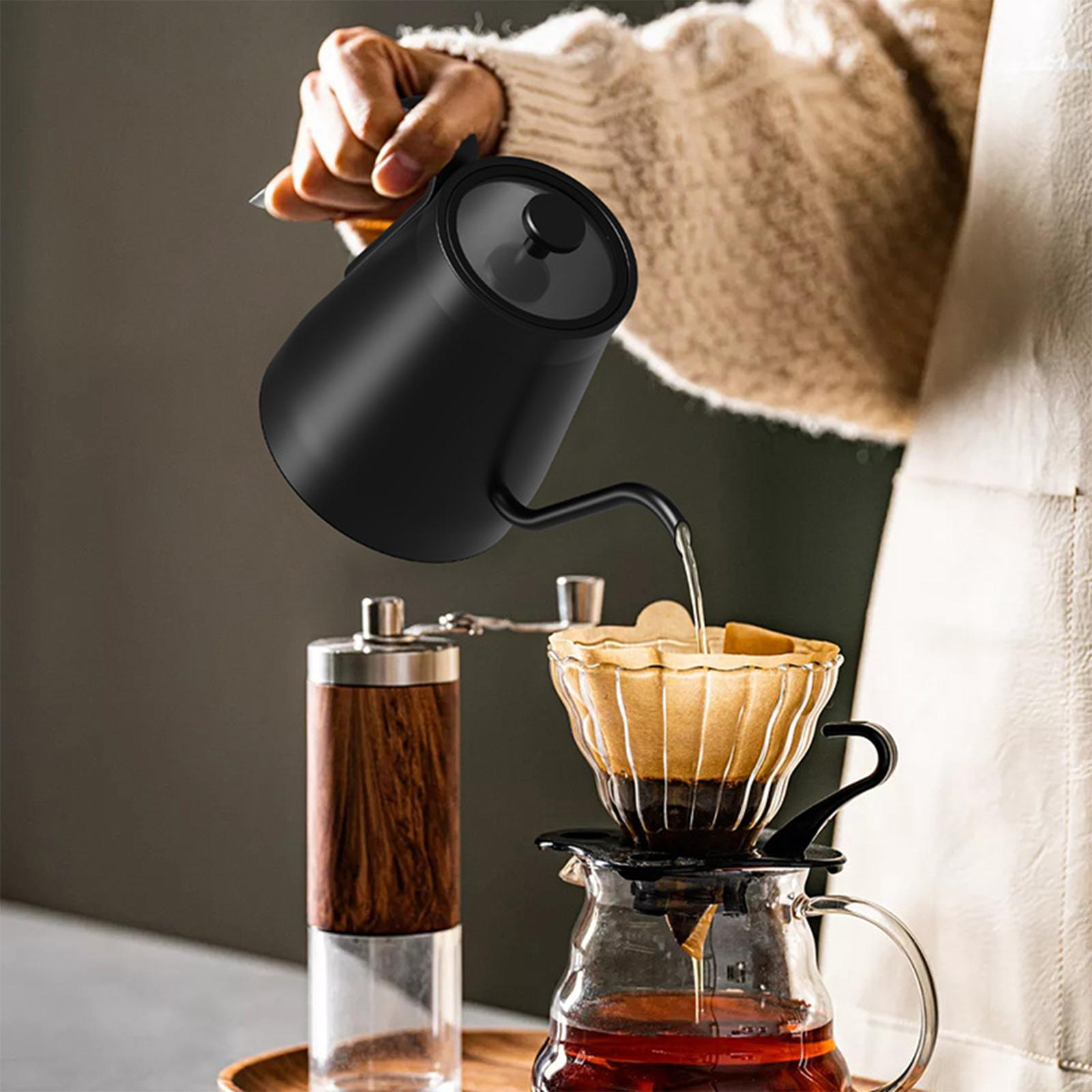 Ein schwarzer Schwanenhalskessel gießt Wasser in einen gläsernen Pour-Over-Kaffeezubereiter, in der Nähe steht eine Holzmühle.