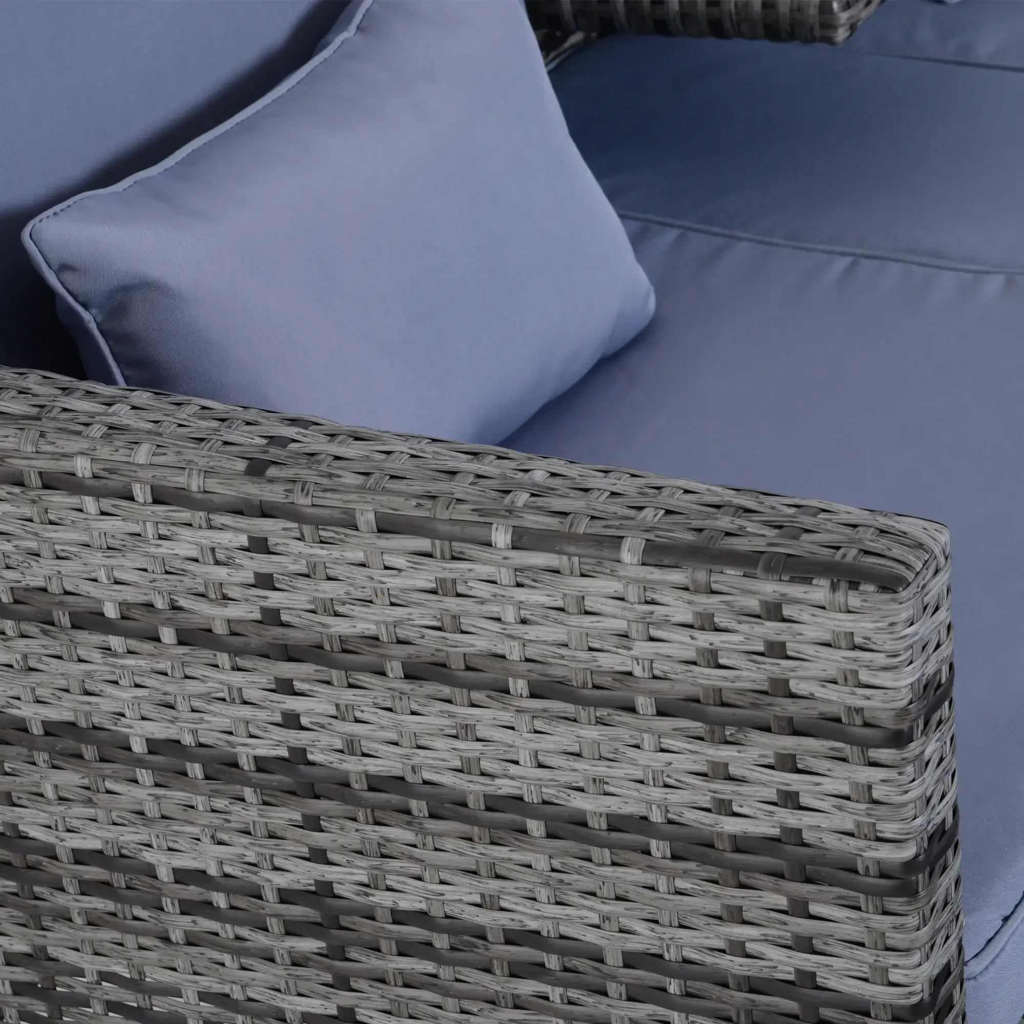 Eine Nahaufnahme, die die Textur von grauem, gewebtem Rattan auf einem Outdoor-Sofa mit hellblauen Kissen zeigt.