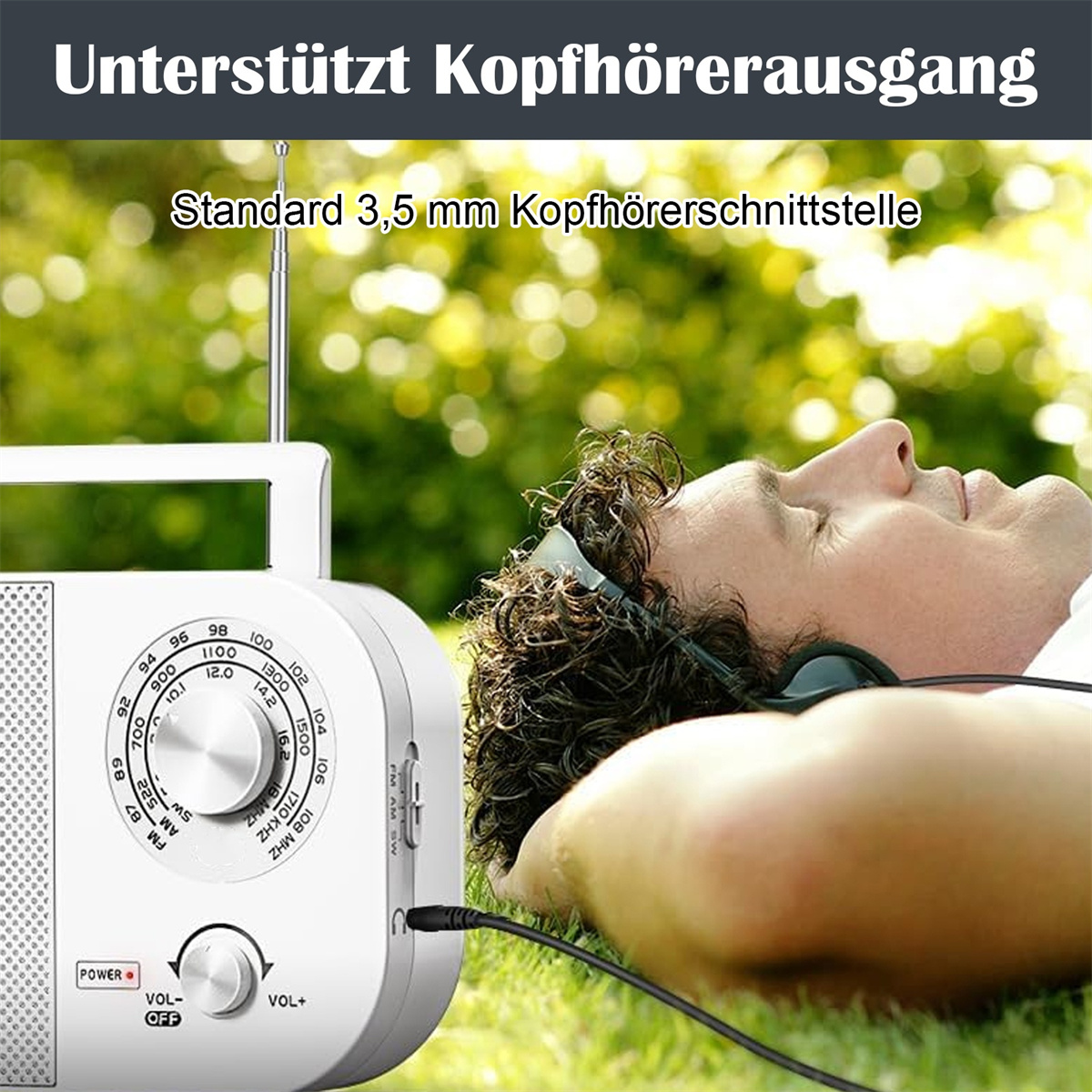 Ein Mann liegt im Gras mit Kopfhörern, die an ein tragbares, weißes Radio angeschlossen sind.