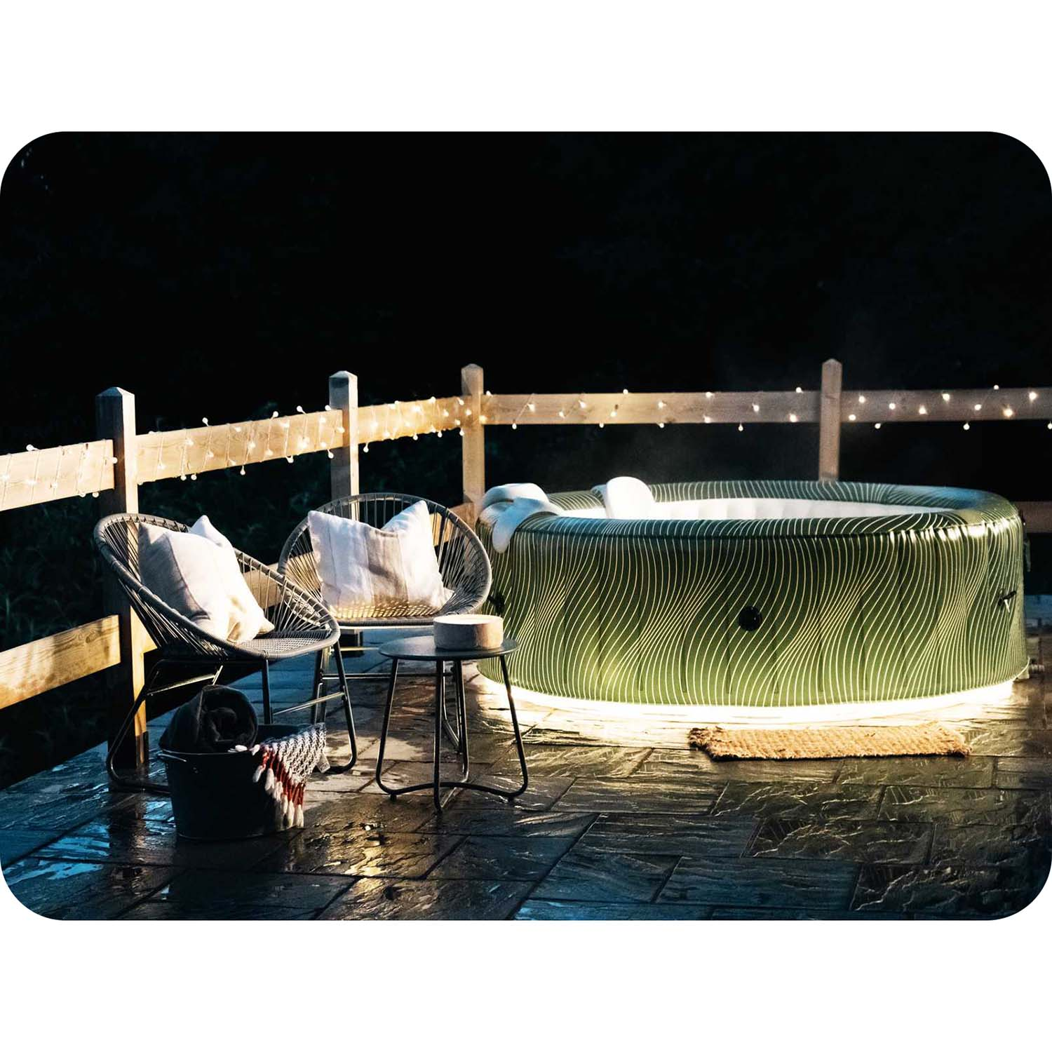 Zewnętrzna wanna z hydromasażem stoi na patio z krzesłami i lampkami, tworząc przytulną atmosferę wieczoru.