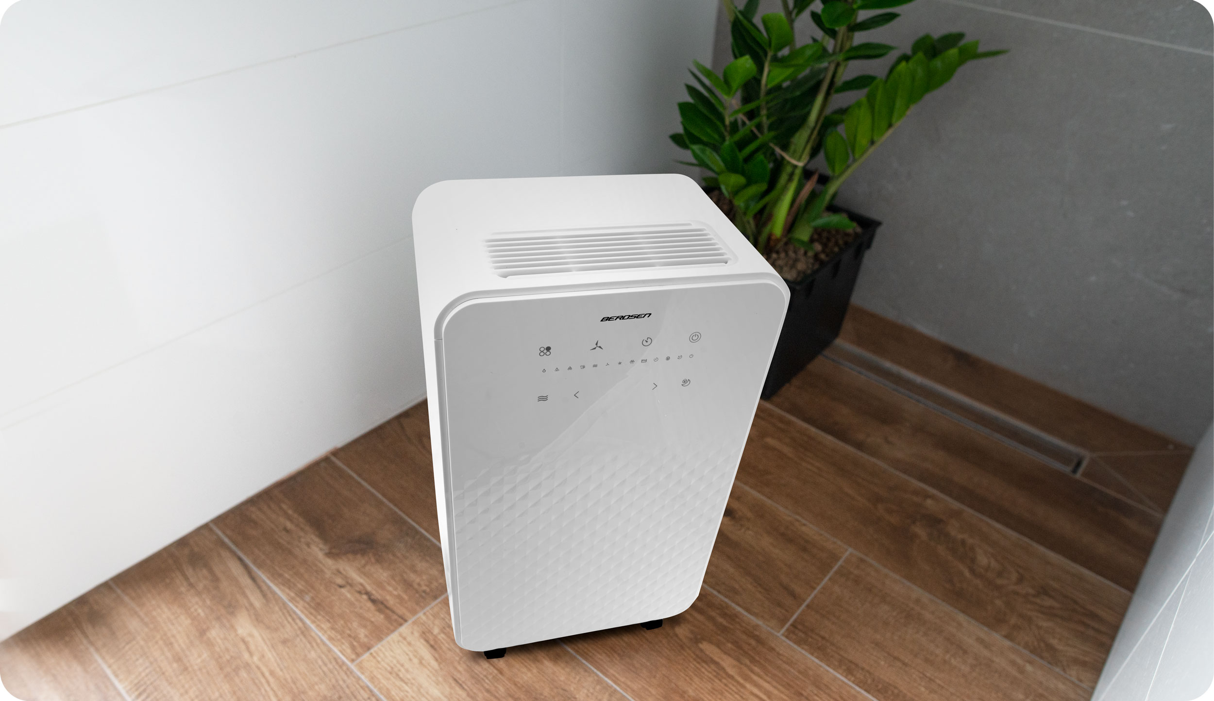 Biały osuszacz powietrza w łazience, obok rośliny i rogu.