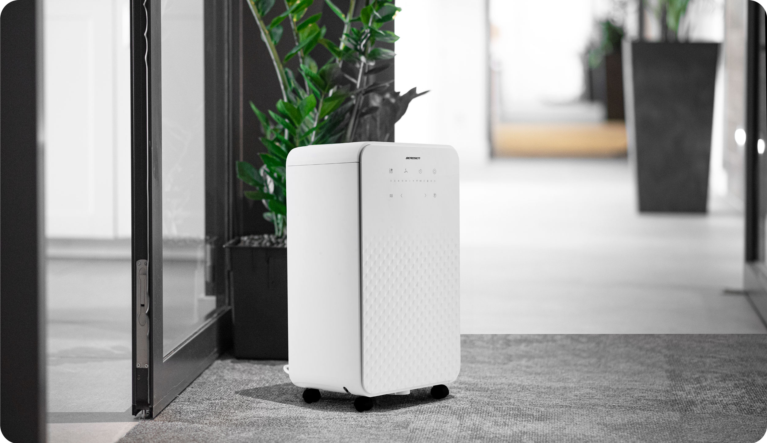 Biały osuszacz powietrza w biurze w pobliżu szklanych drzwi i roślin.