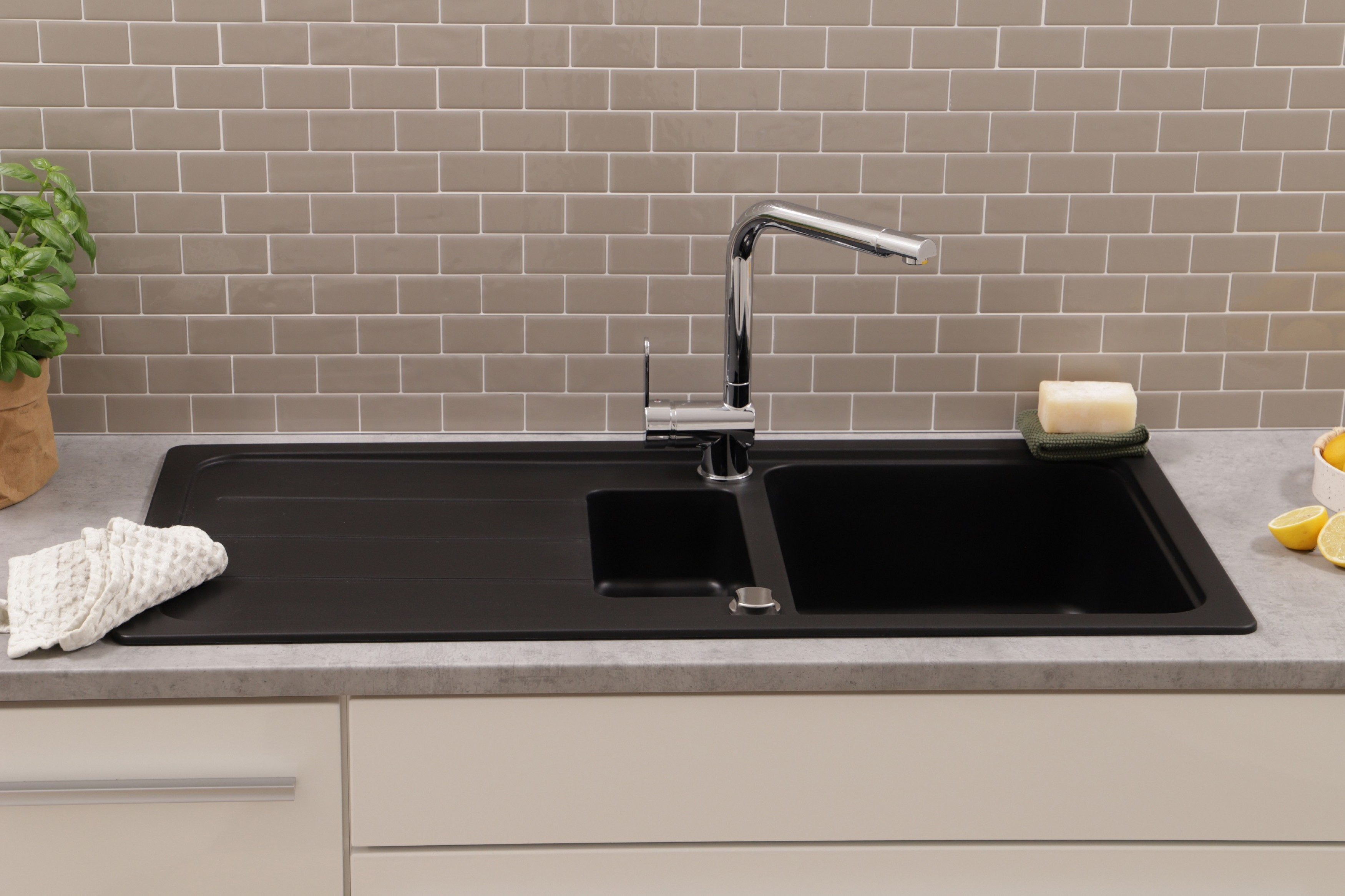 Ein schwarzes Waschbecken mit einem Wasserhahn, Zitronen und einem Schwamm auf einer grauen Arbeitsplatte.