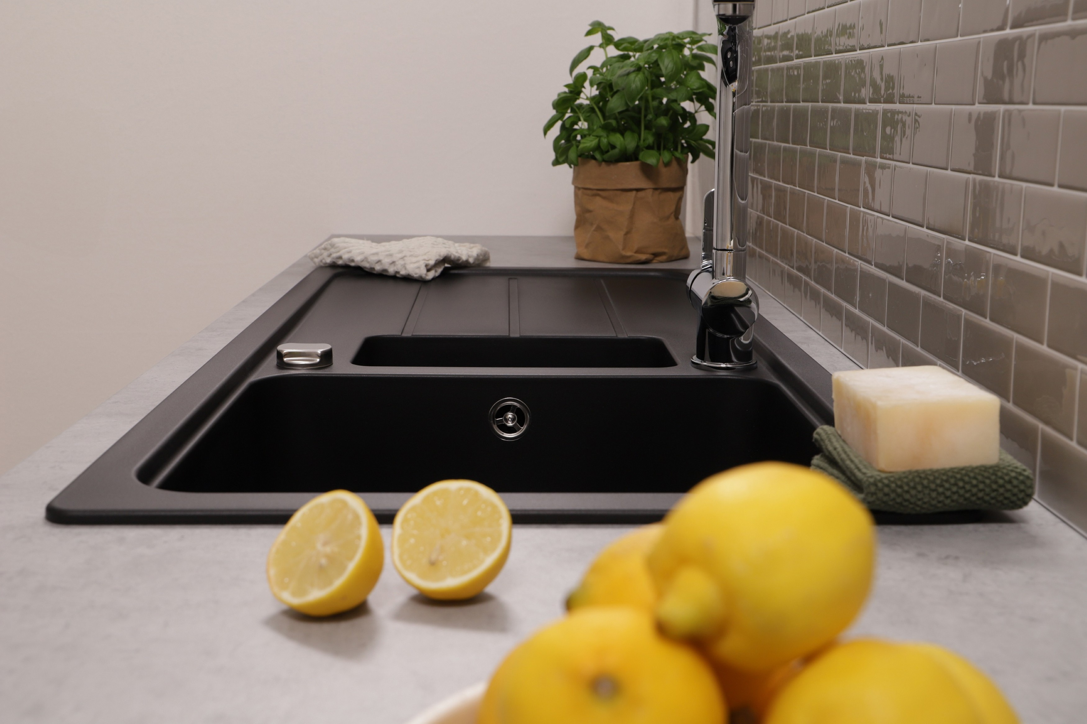 Ein schwarzes Waschbecken mit Zitronen und einem Schwamm auf einer grauen Arbeitsplatte, Nahaufnahme.
