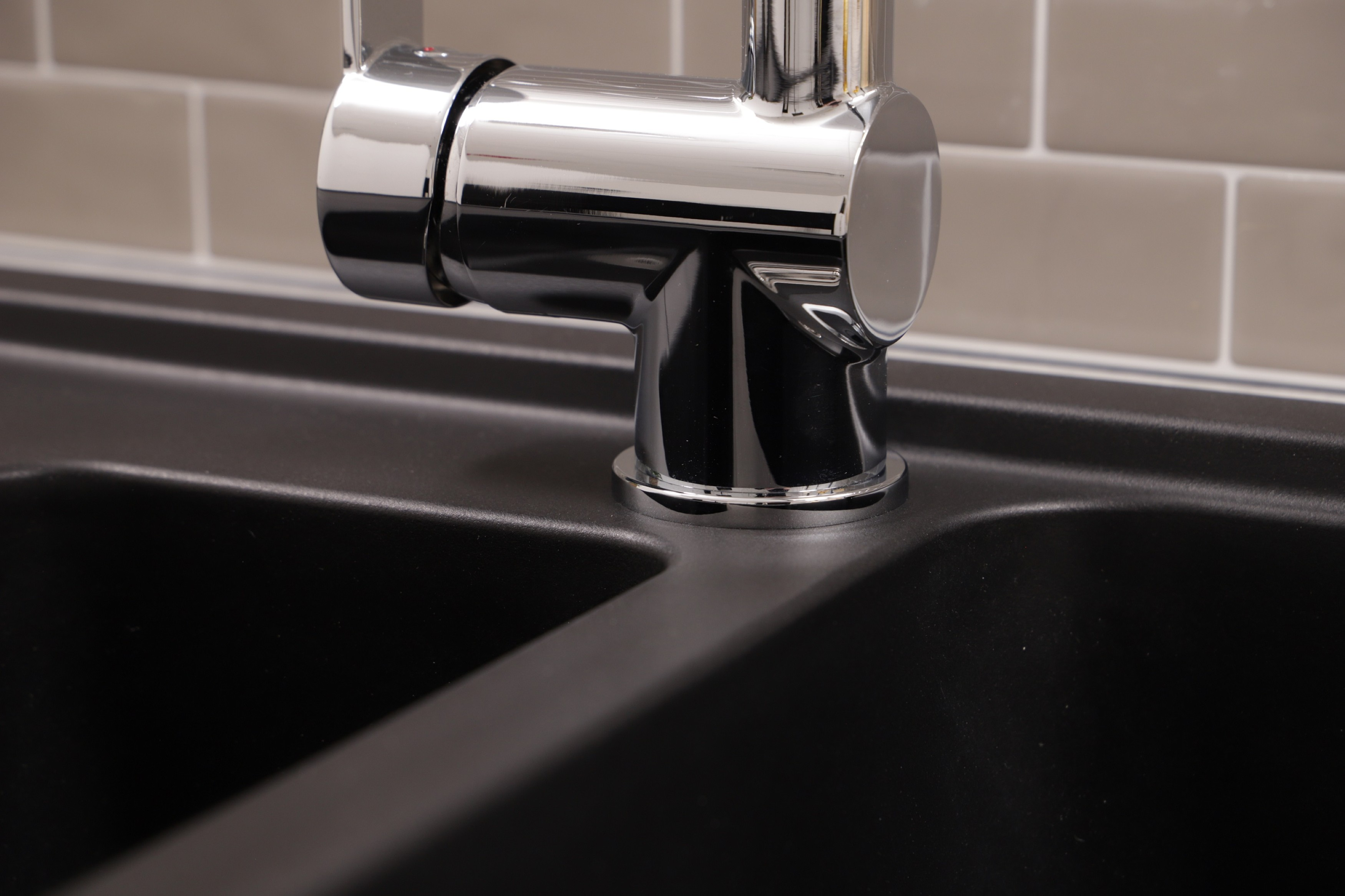 Eine Nahaufnahme eines glänzenden Wasserhahns auf einem schwarzen Waschbecken.