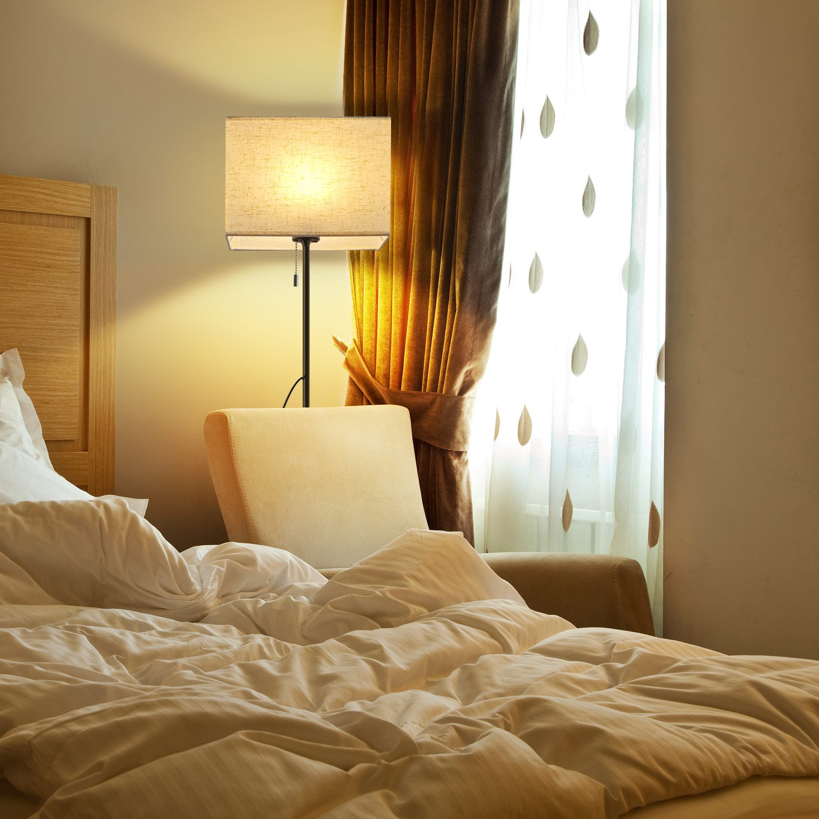 Una camera da letto con letto, sedia, lampada da terra e finestra con tende.
