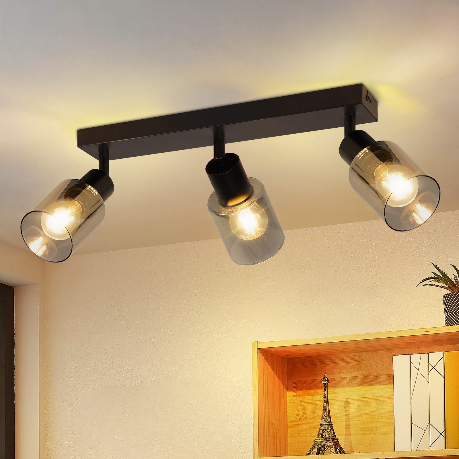 Una plafoniera con tre lampadine ha paralumi in vetro trasparente e un attacco nero su una parete neutra.
