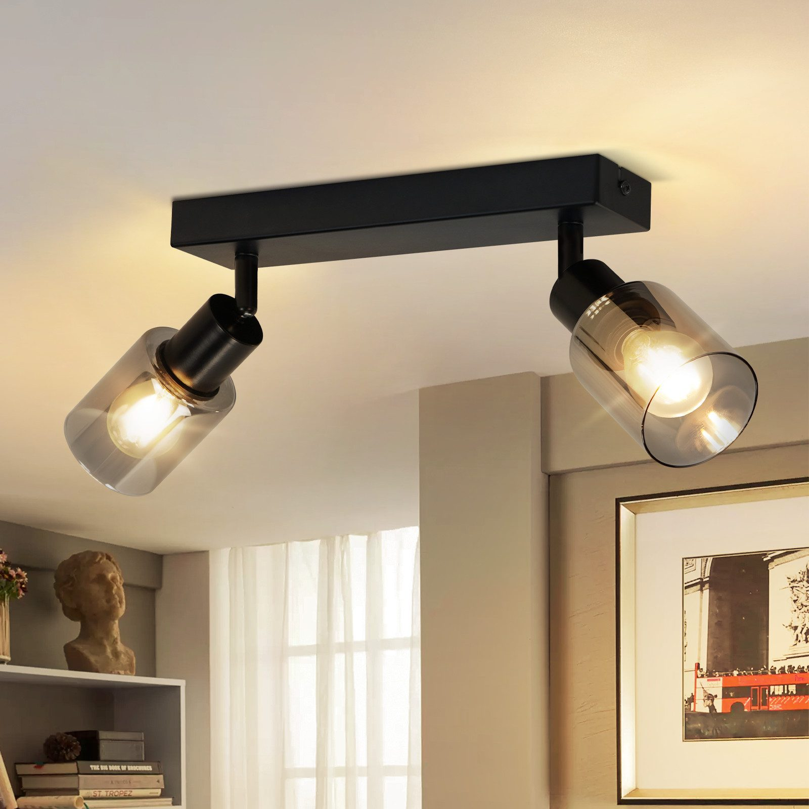 Un lampadario nero con due lampadine ha paralumi in vetro trasparente in una stanza con un busto e opere d'arte.