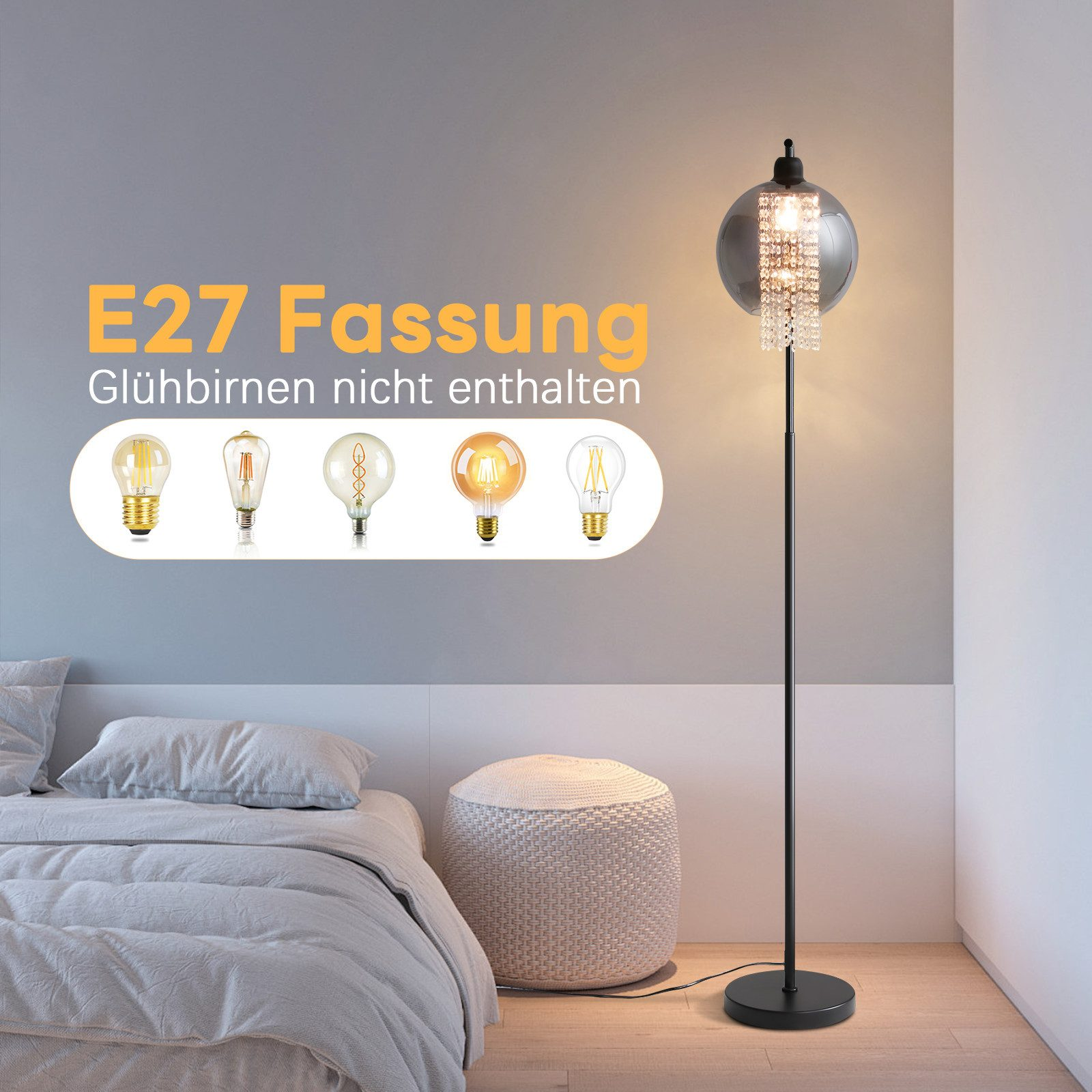 Eine Stehlampe mit einem grauen kugelförmigen Schirm und Kristallakzenten neben einem Bett mit Kissen.