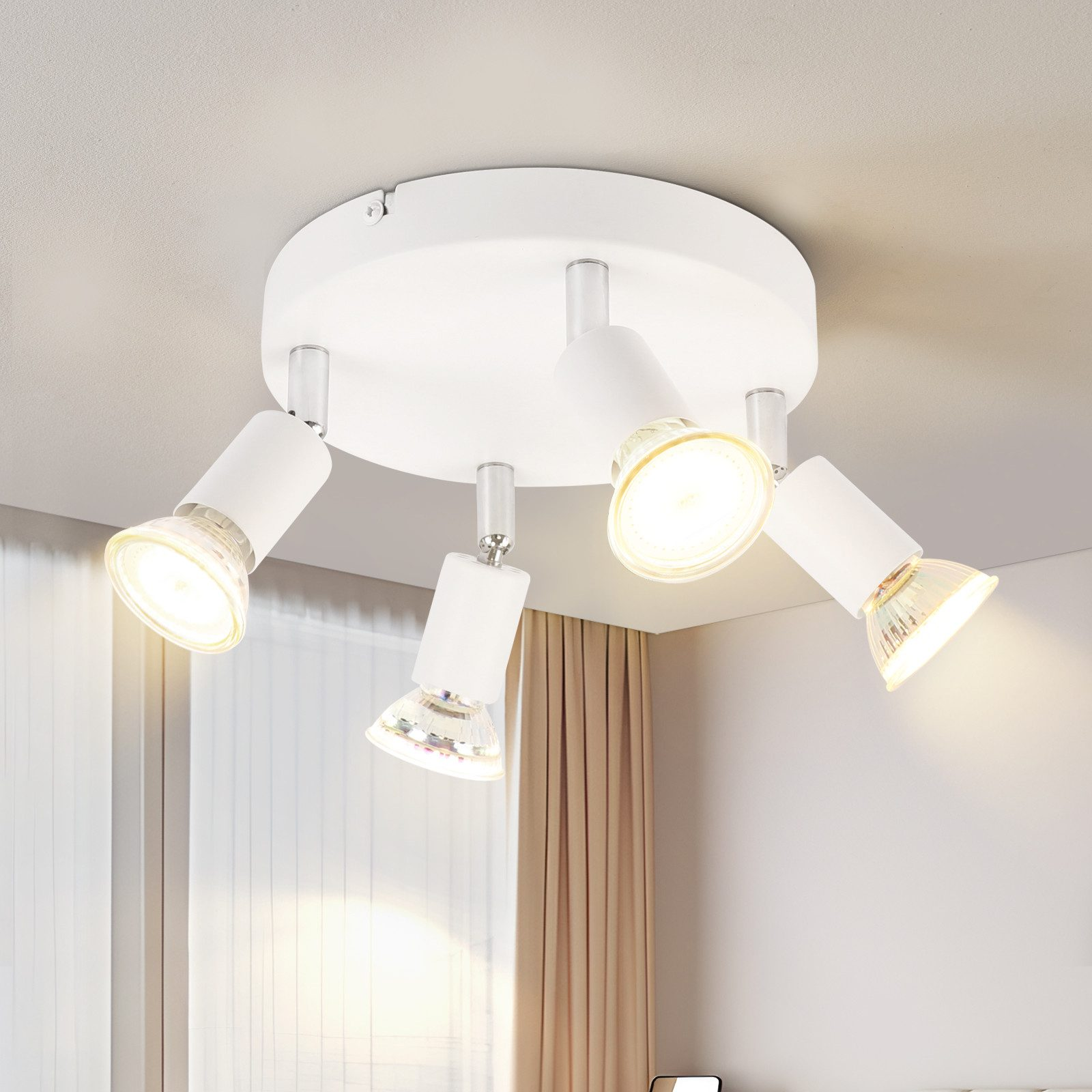 Una plafoniera bianca con quattro faretti regolabili illumina una stanza con tende beige.