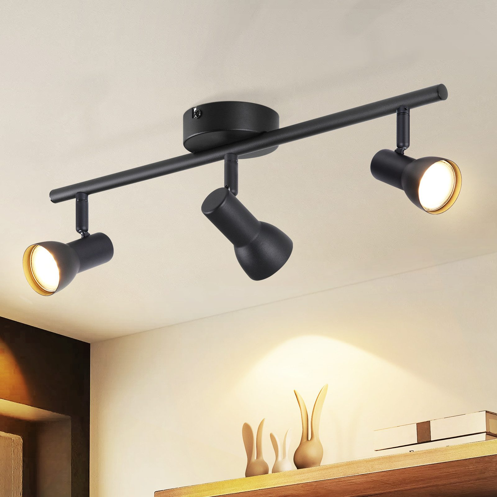 Una lampada da binario nera con tre faretti illumina una mensola con figure decorative di coniglietti in un ambiente accogliente.