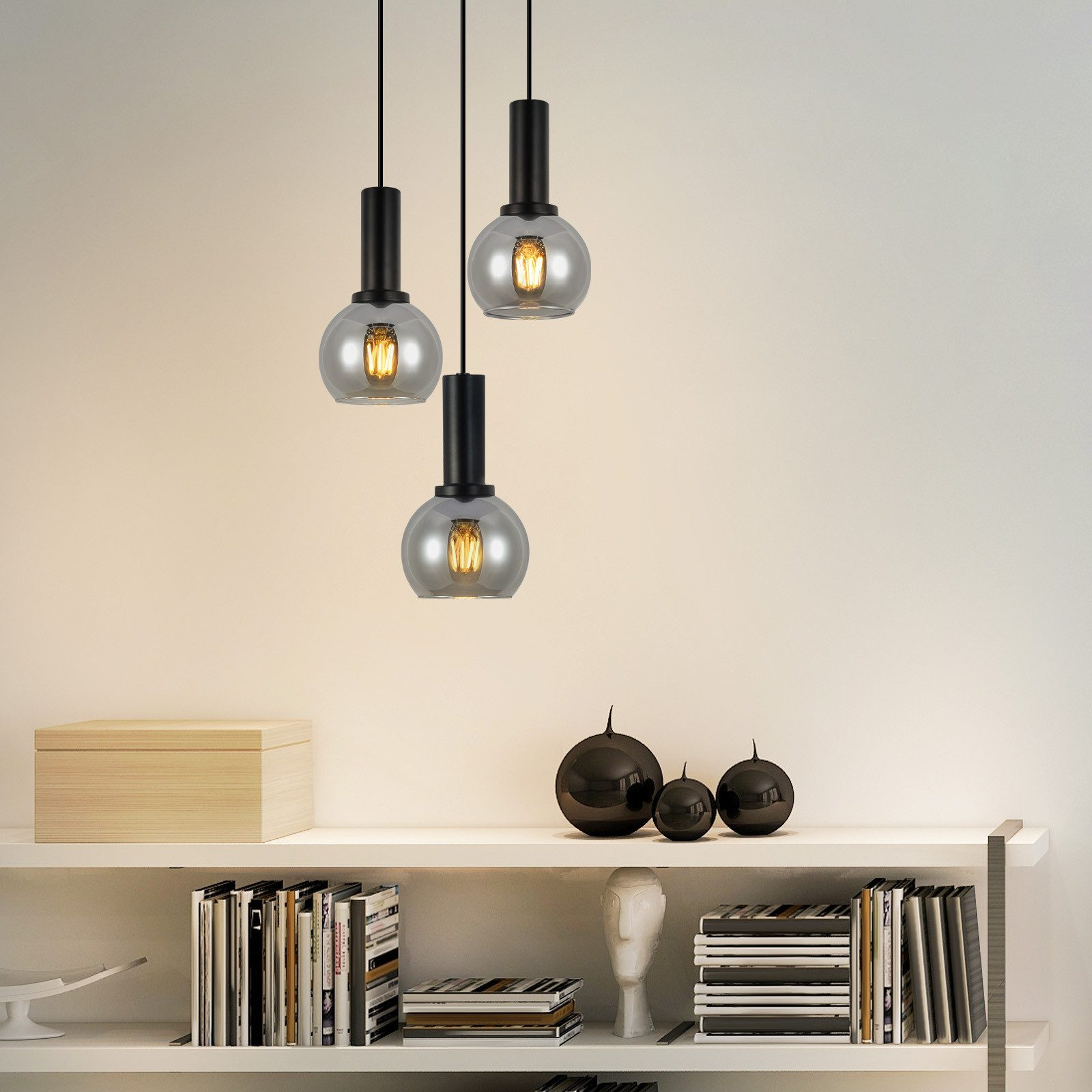 Trzy lampy wiszące z kloszami z przydymionego szkła wiszące nad półką z książkami i przedmiotami dekoracyjnymi, prezentujące wystrój wnętrz.