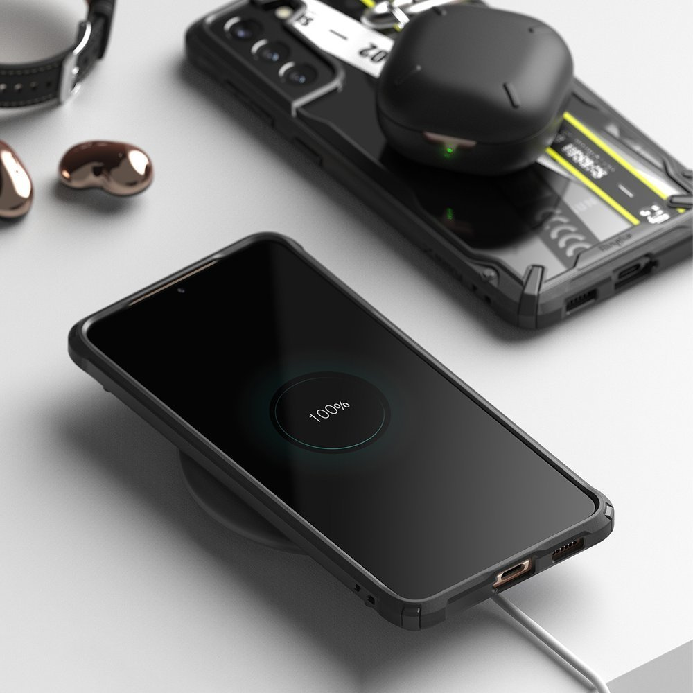 Czarny smartfon ładuje się bezprzewodowo z pobliskim etui na słuchawki. Ekran telefonu pokazuje 100% naładowania.