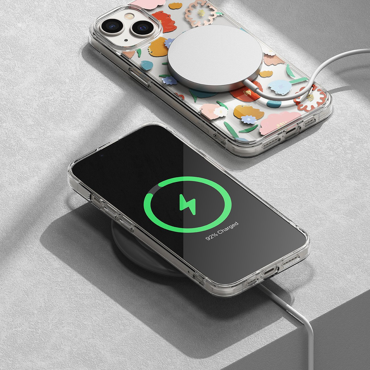 Dwa telefony ładujące się bezprzewodowo na białej powierzchni, jeden z kwiatowym etui.