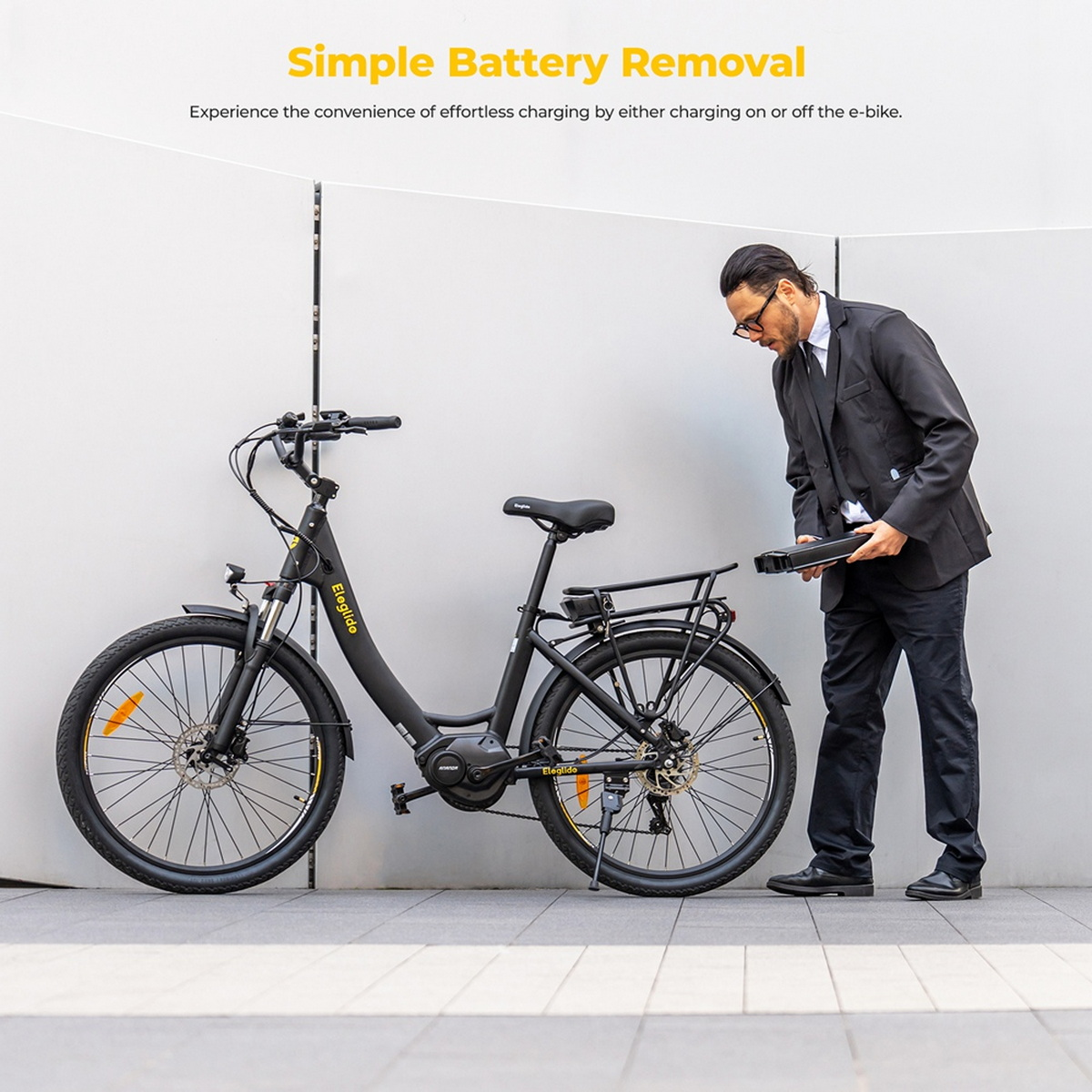 Eine Person entfernt die Batterie eines schwarzen E-Bikes. Das Fahrrad ist an einer hellgrauen Wand geparkt.