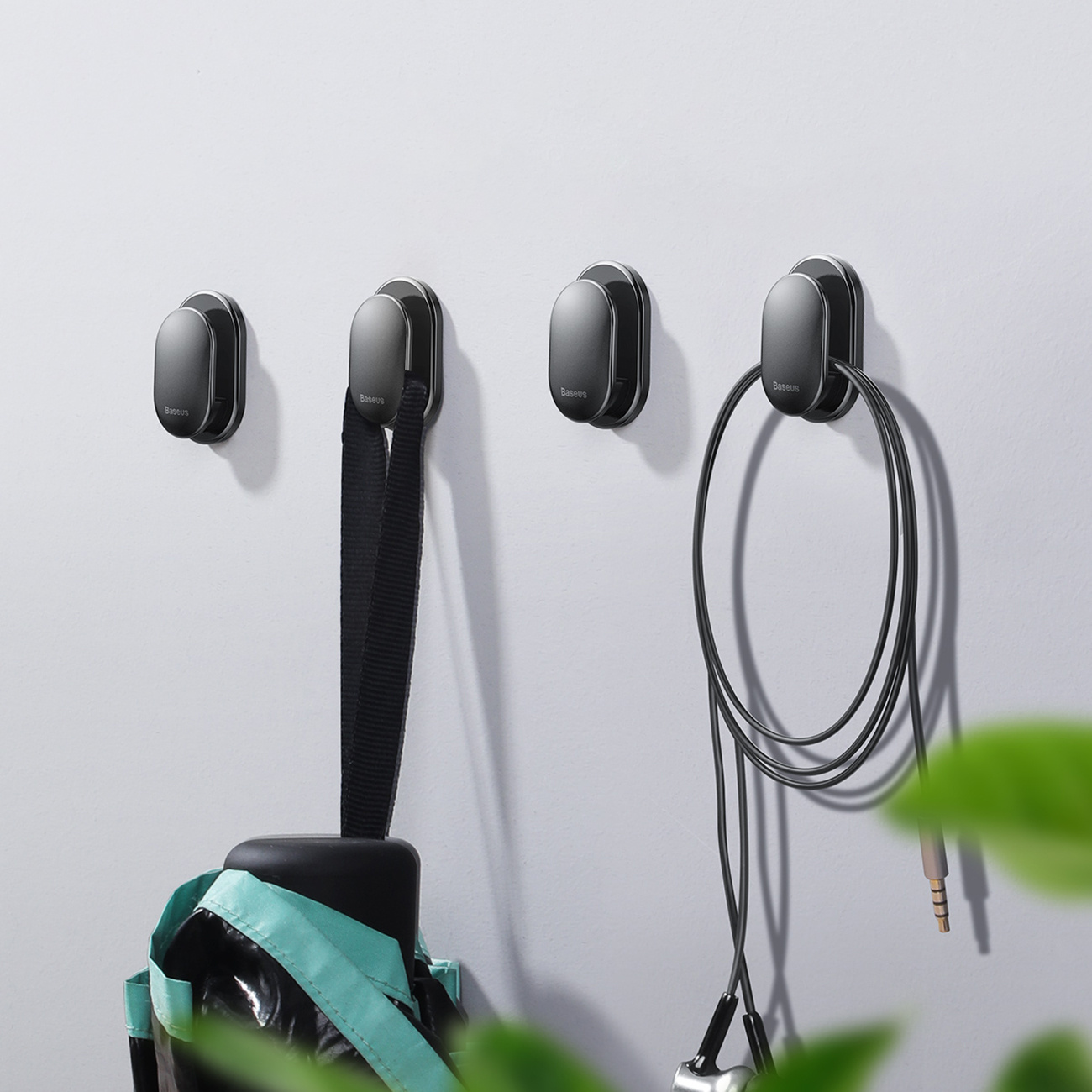 Cztery haczyki Baseus są zamontowane na białej ścianie, trzymając parasol i kable, prezentując ich użyteczność i design.