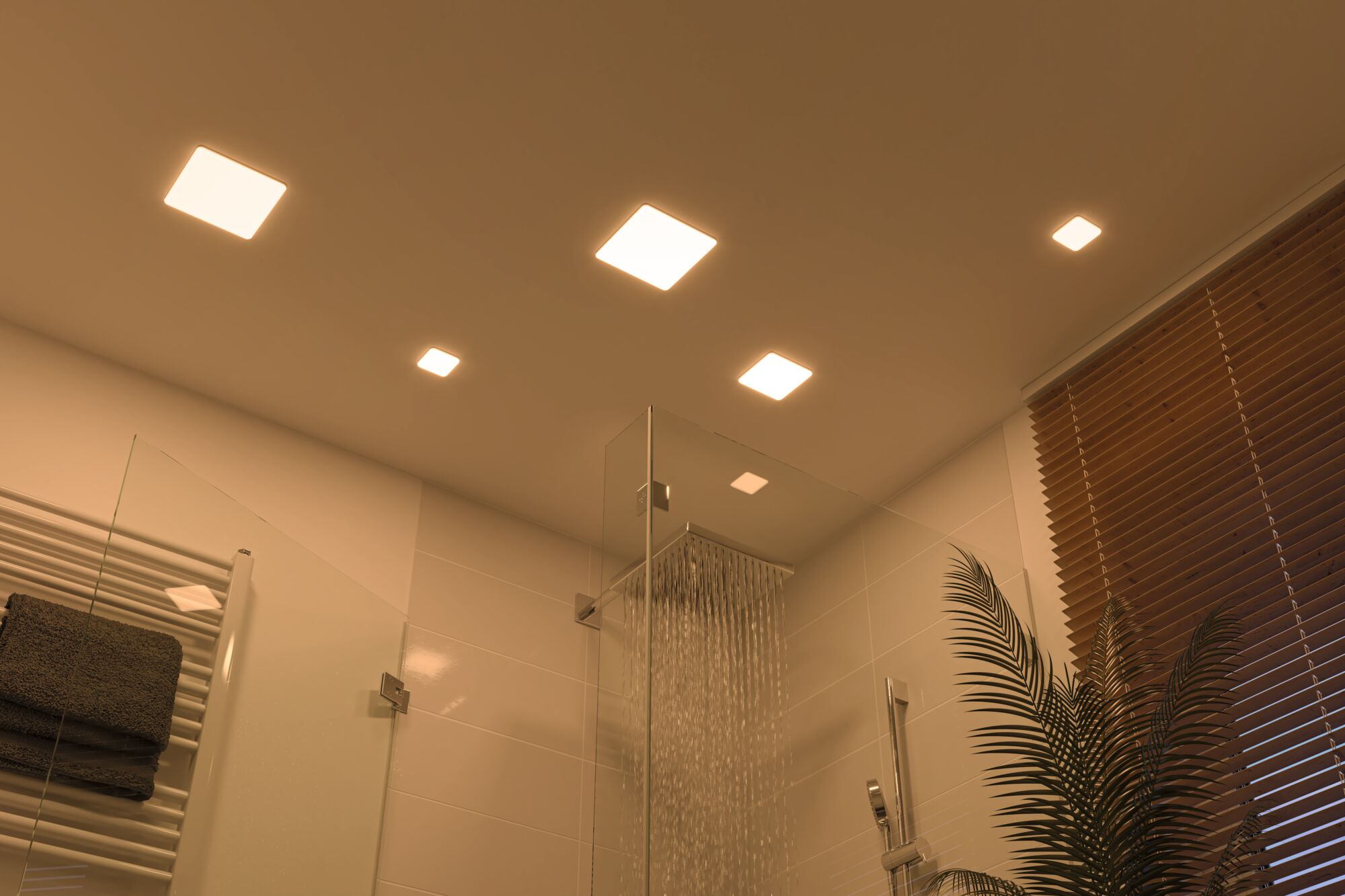 Badezimmer mit Dusche, gefliesten Wänden, Jalousien und quadratischen Deckenleuchten.
