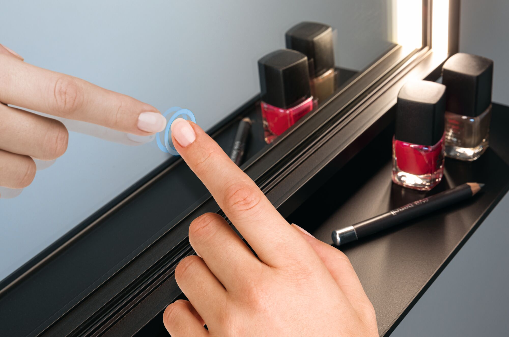 Palce dotykają lustra, na którym wyeksponowane są kosmetyki. Scena skupia się na interakcji z lustrem i układzie produktów.