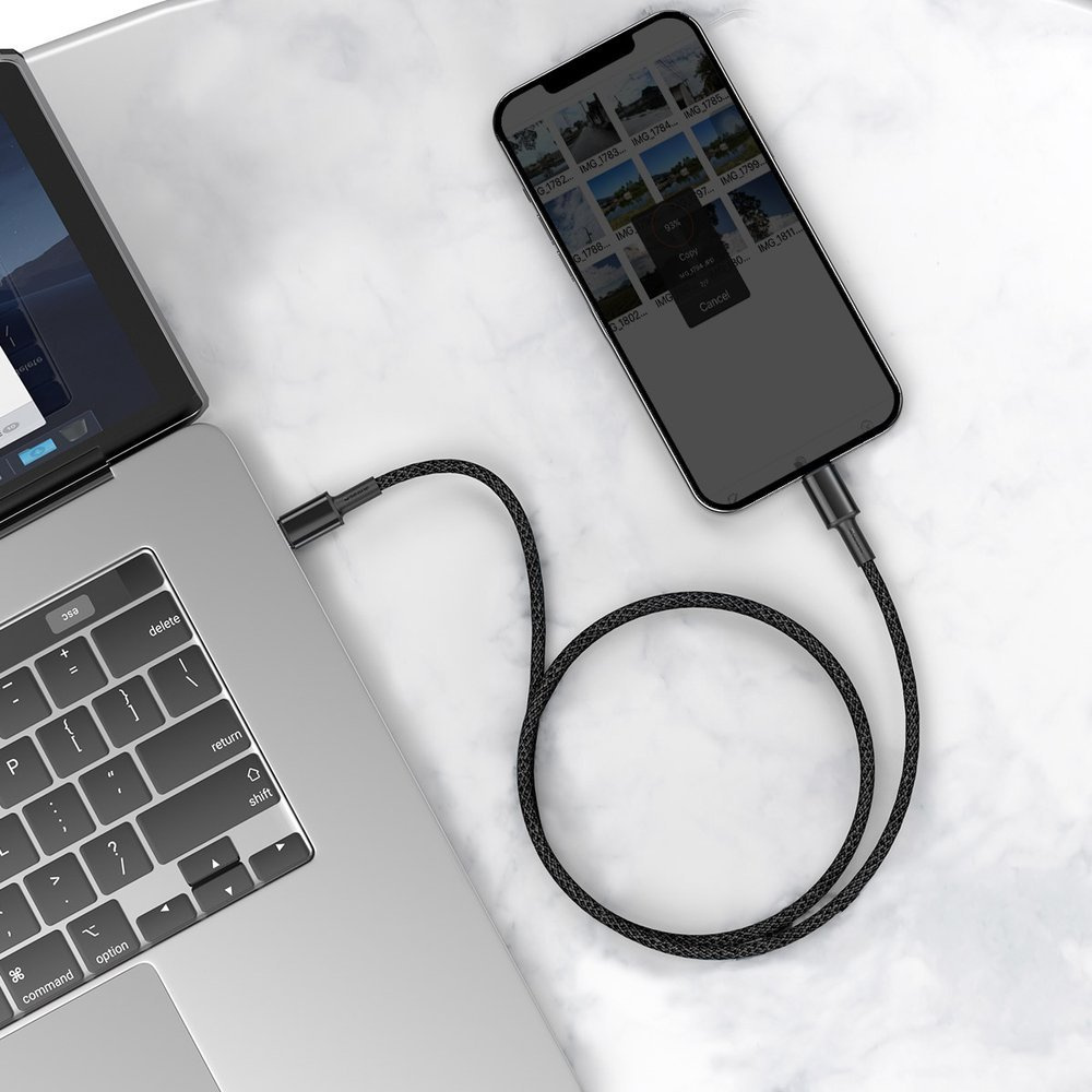 Telefon jest podłączony do laptopa za pomocą czarnego kabla. Telefon wyświetla obrazy. Marmurowa powierzchnia.