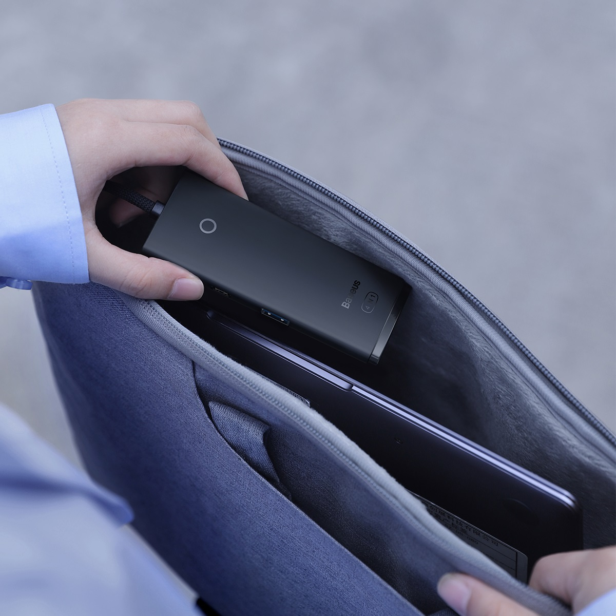 Osoba wkłada czarny hub USB Baseus do szarej torby z laptopem.