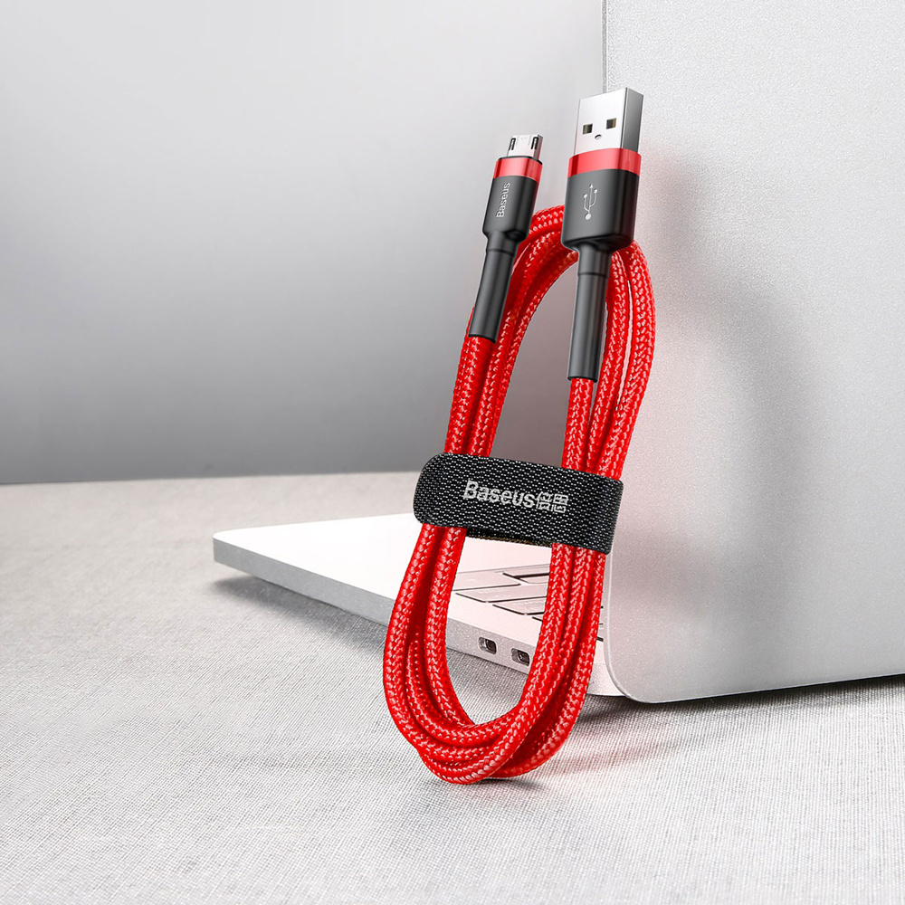 Czerwony kabel USB ze złączami USB-A i micro-USB, owinięty i trzymany przez czarny pasek, blisko laptopa.